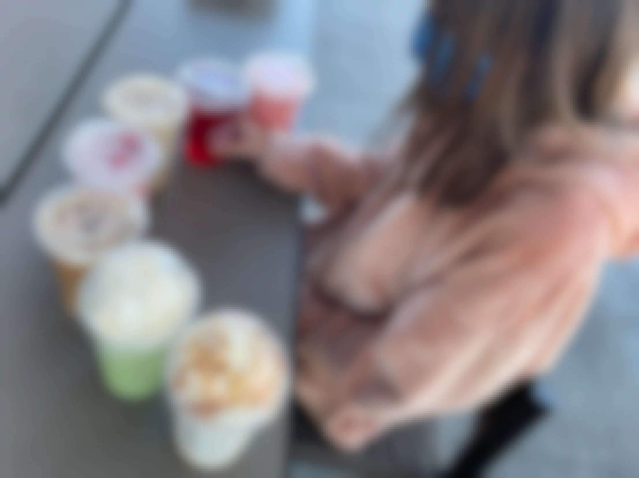 A young girl sitting at a table with a row of Starbucks secret menu drinks in front of her.