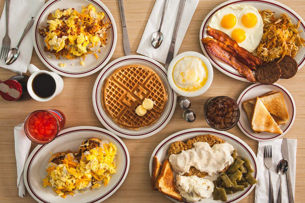 A table of breakfast menu items from Huddle House including waffles, pancakes, eggs, toast, bacon, sausage, and some drinks.