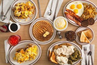 A table of breakfast menu items from Huddle House including waffles, pancakes, eggs, toast, bacon, sausage, and some drinks.