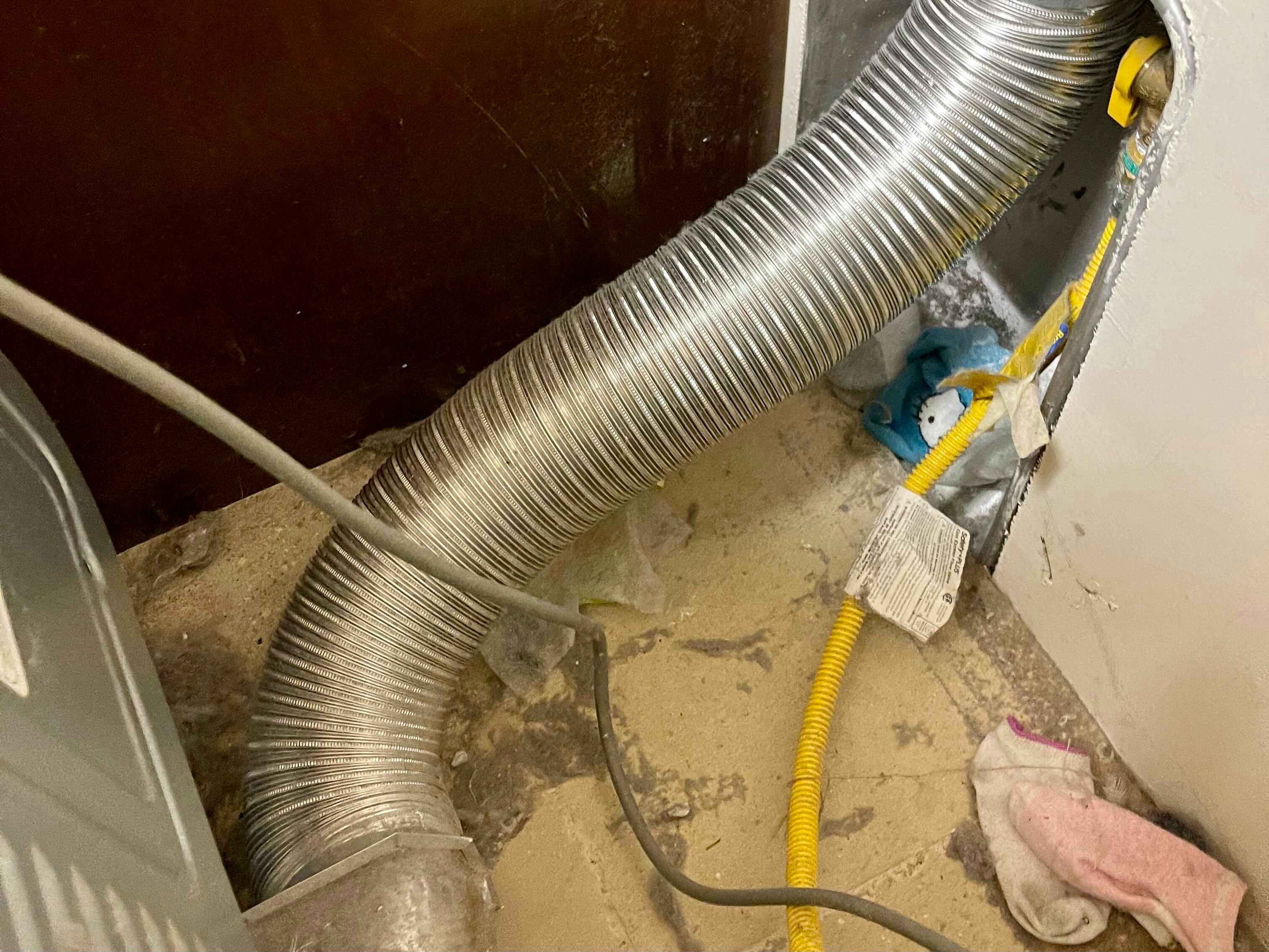 Dryer pulled out from wall to show dryer hose in back of dyer with lost socks, lint, and dust
