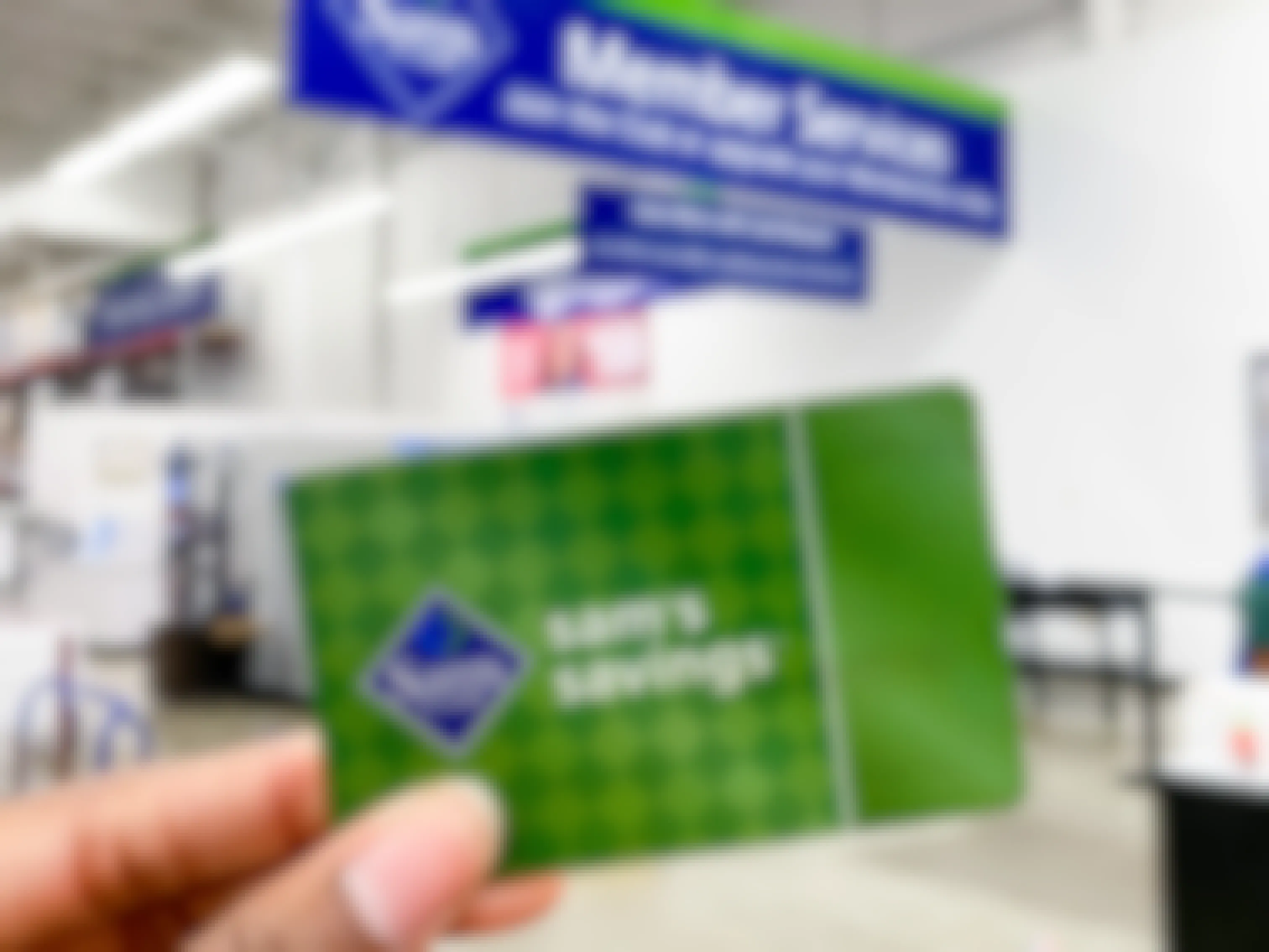 A person holding a Sam's Club membership card in front of the Member Services desk inside Sam's Club.