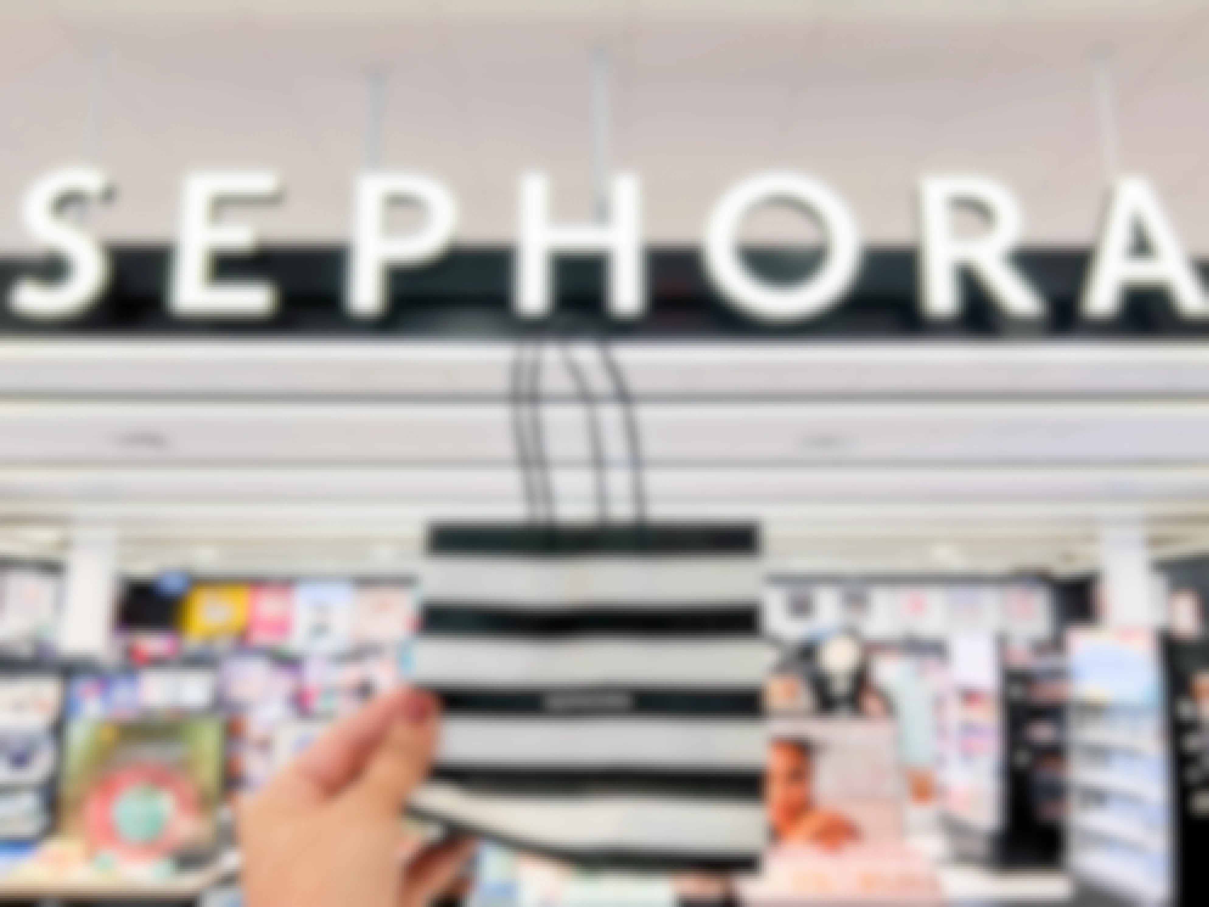 A person's hand holding a Sephora shopping bag outside of a Sephora store.