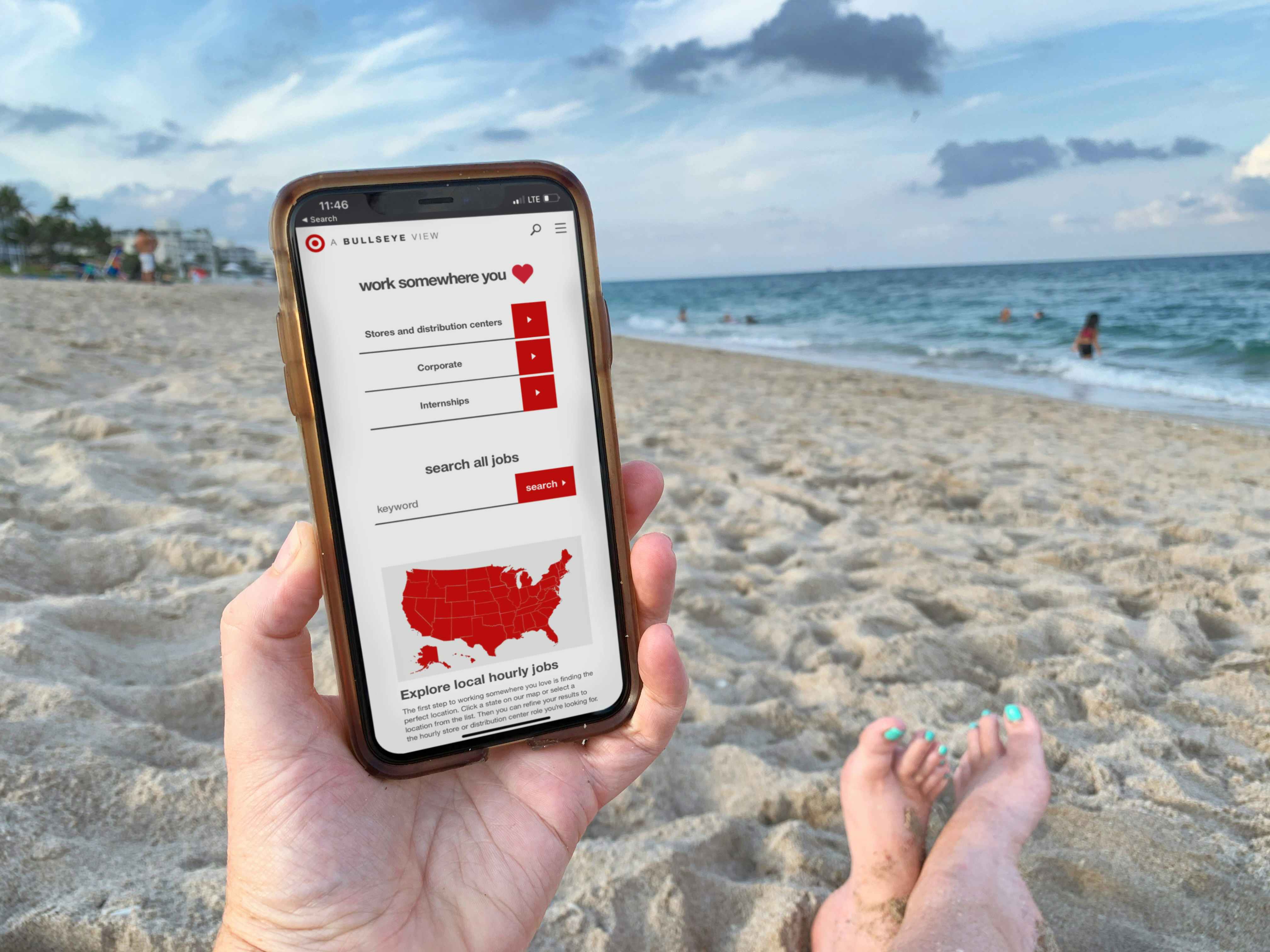 person sitting on the beach holding a cellphone with target employee website on screen