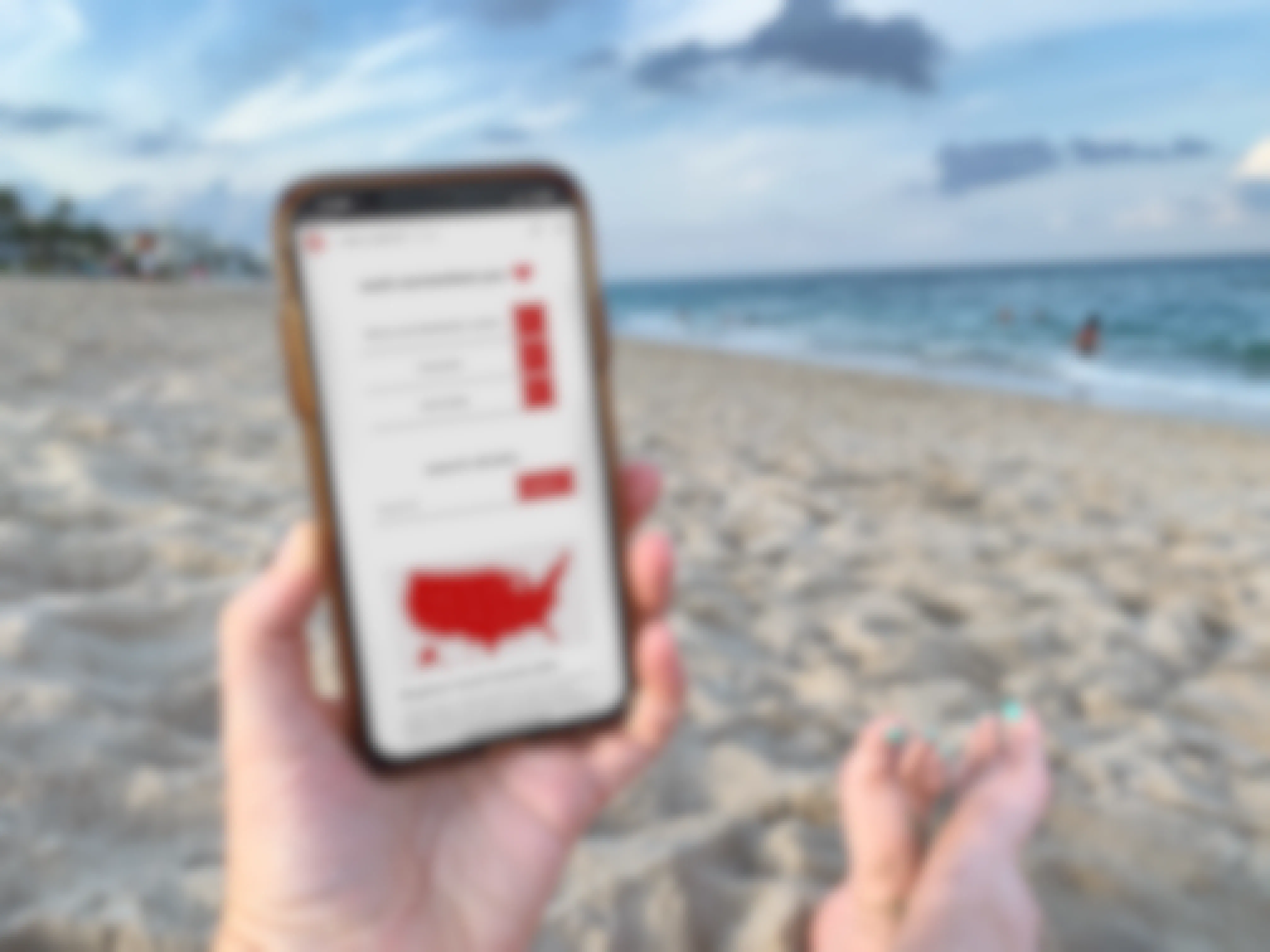 person sitting on the beach holding a cellphone with target employee website on screen