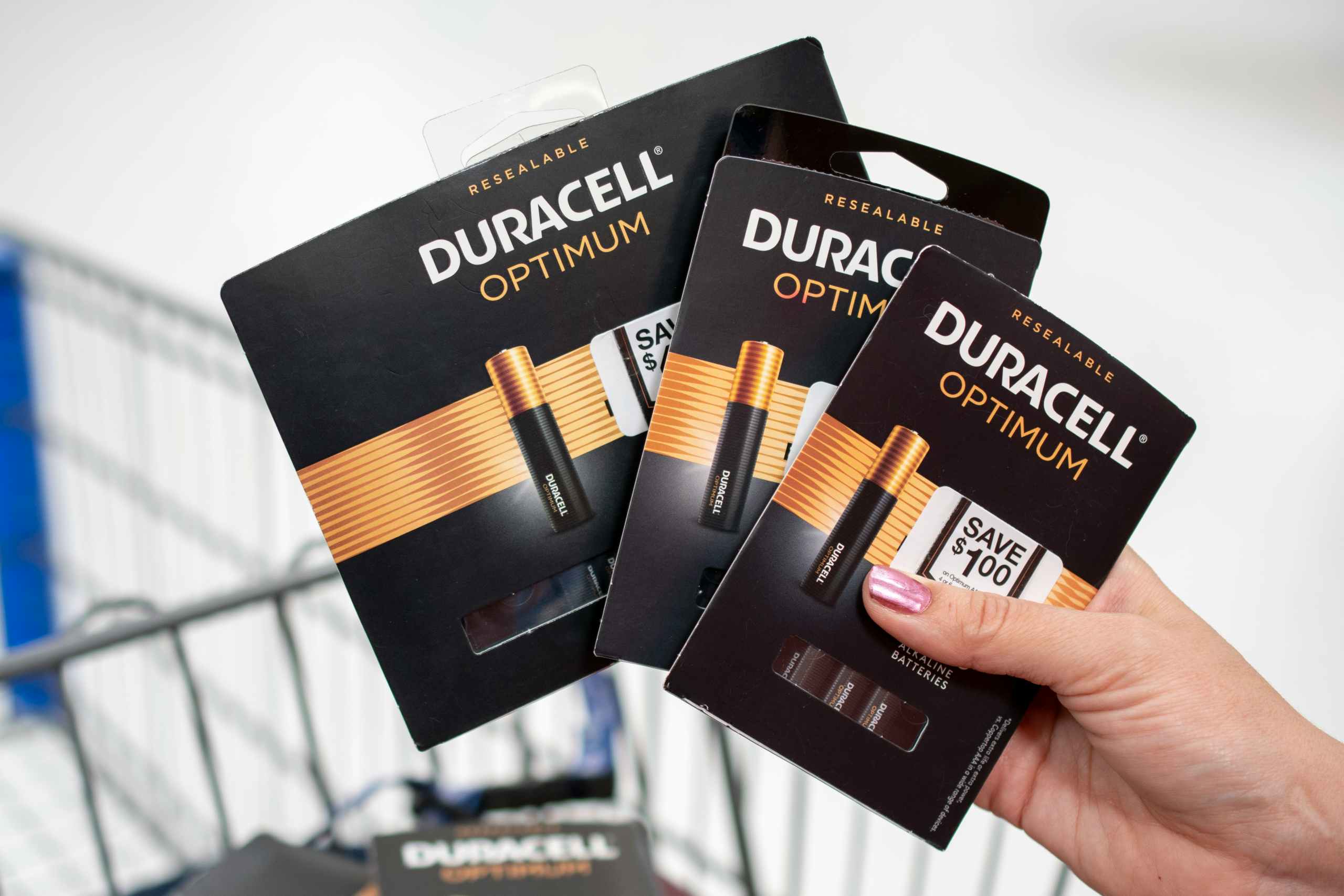 A person holding packages of Duracell Optimum batteries