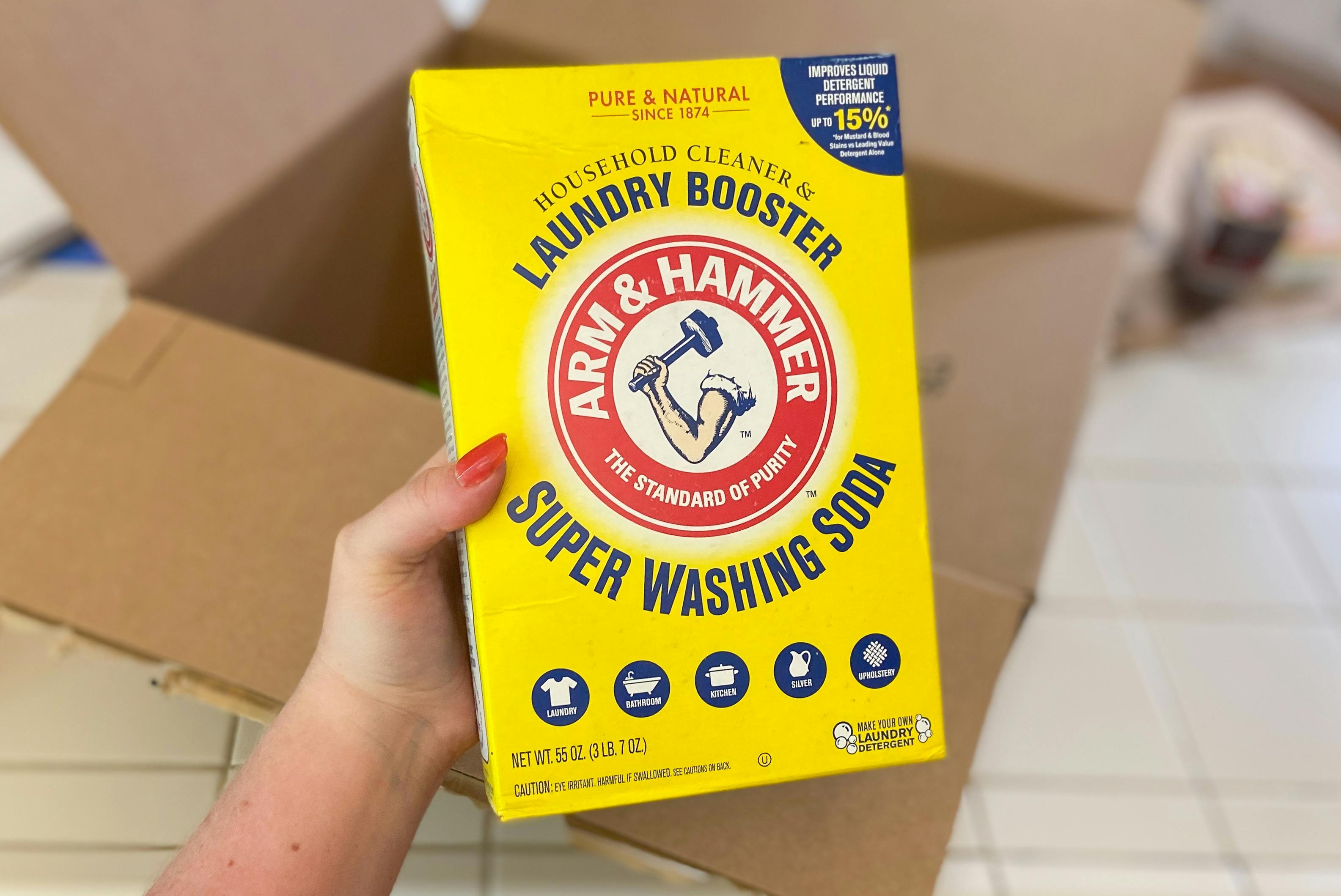 hand holding arm and hammer laundry booster super washing soda in front of an amazon box