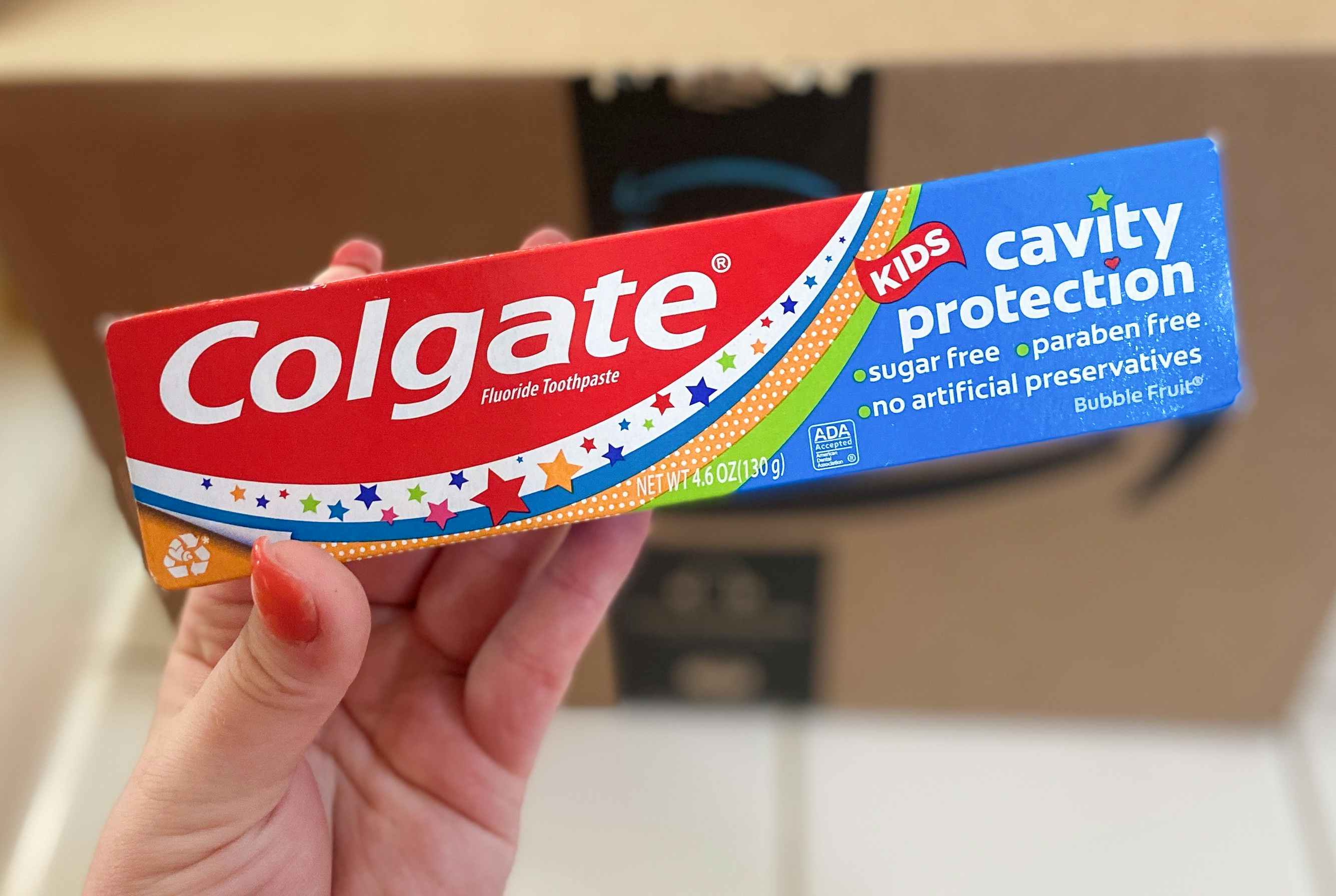 hand holding colgate cavity protection kids toothpaste in front of an amazon box
