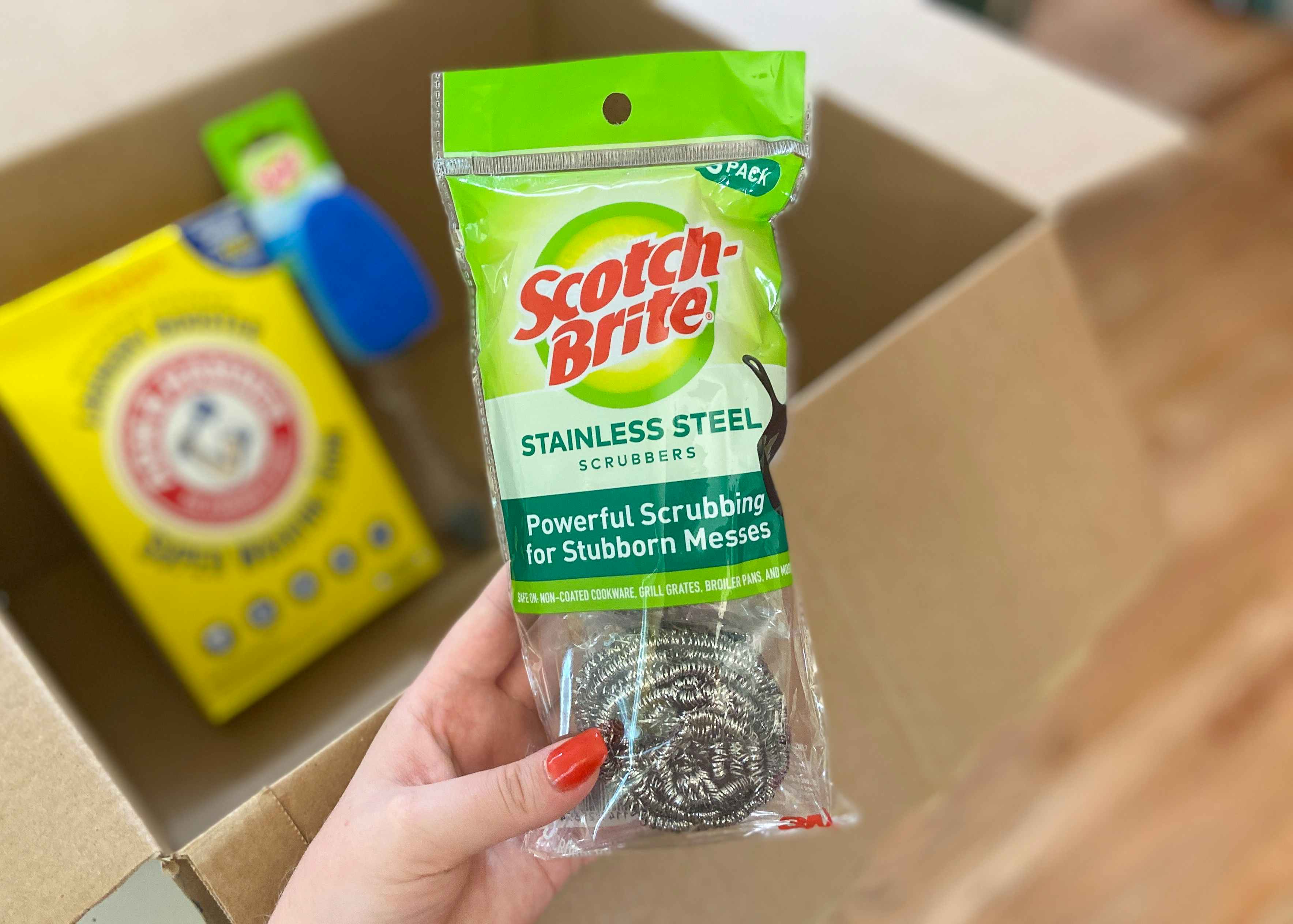 hand holding scotch brite stainless steel scrubbers in front of an amazon box