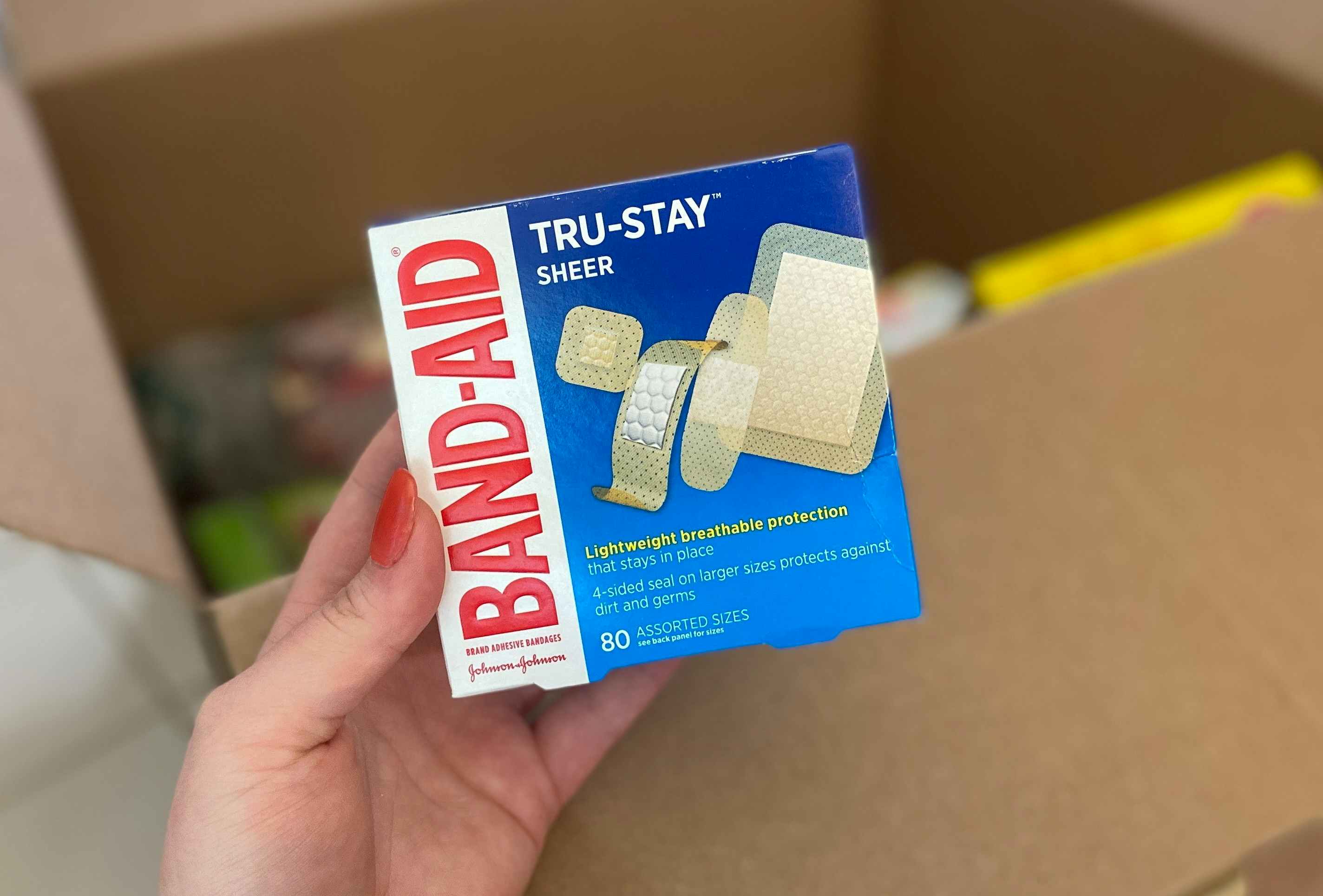 hand holding band aid true stay sheer bandages in front of a box