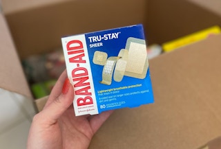 hand holding band aid true stay sheer bandages in front of a box