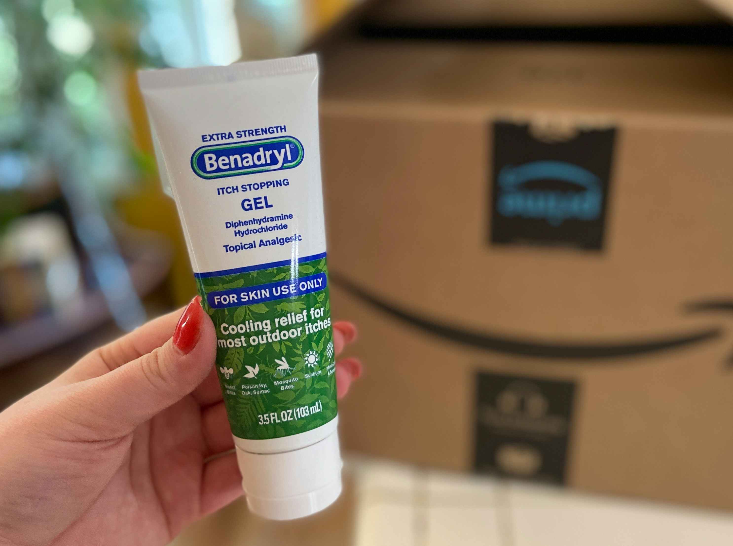 hand holding benadryl anti-itch gel cream in front of an amazon box