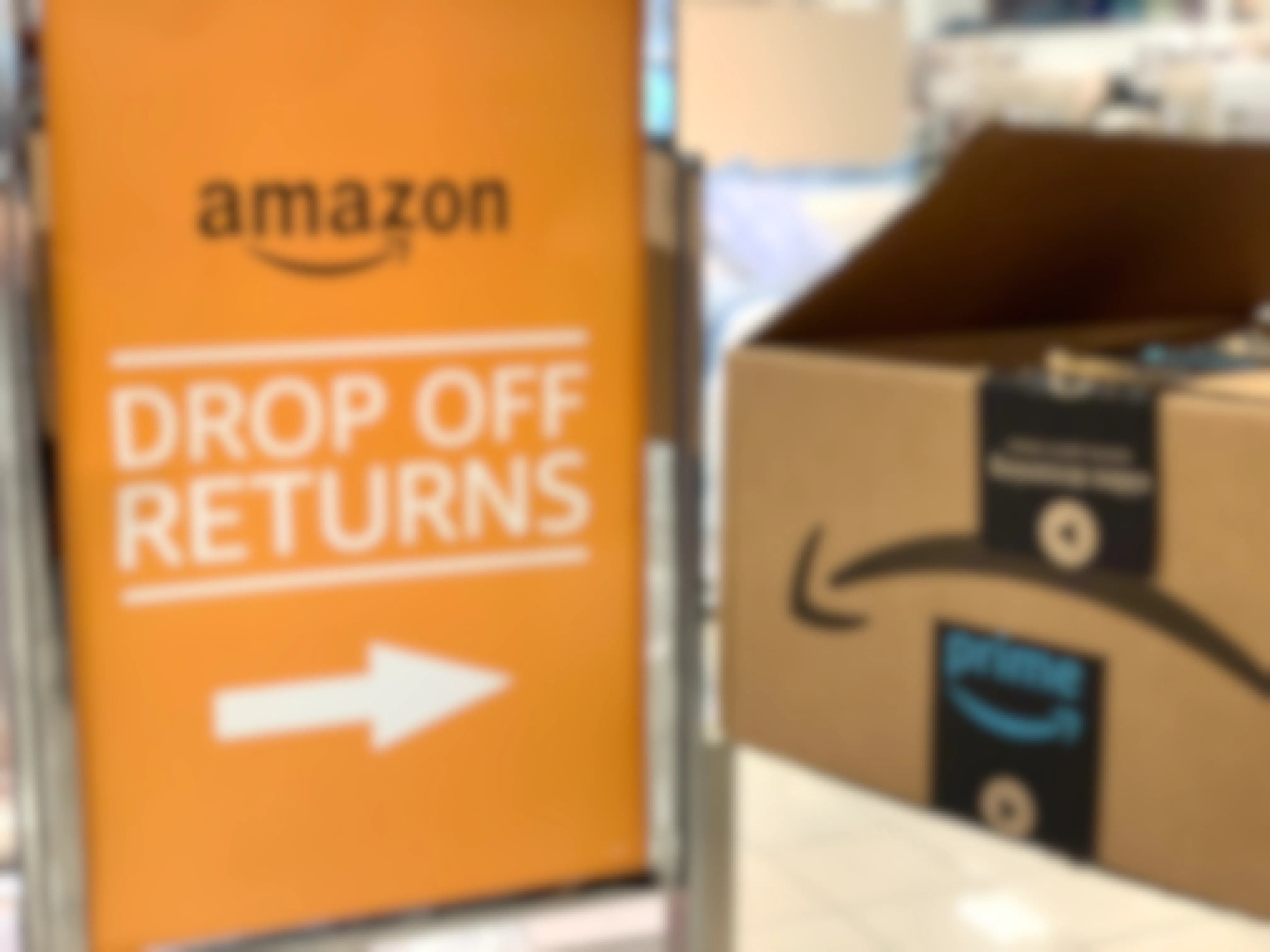 An Amazon box being held up next to a sign directing where to drop off Amazon returns at Kohl's.