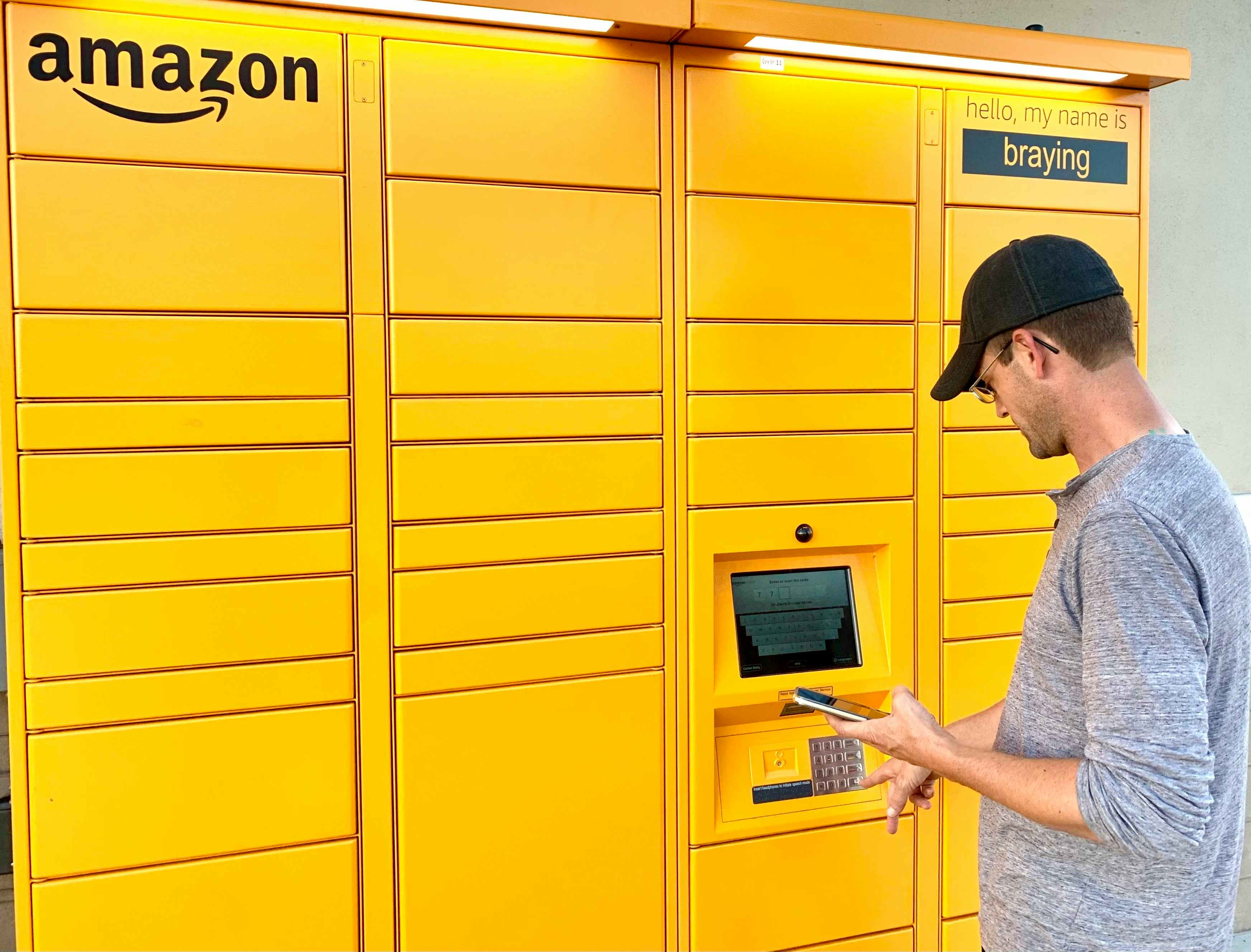 man looking at cellphone while typing on amazon hub locker keypad