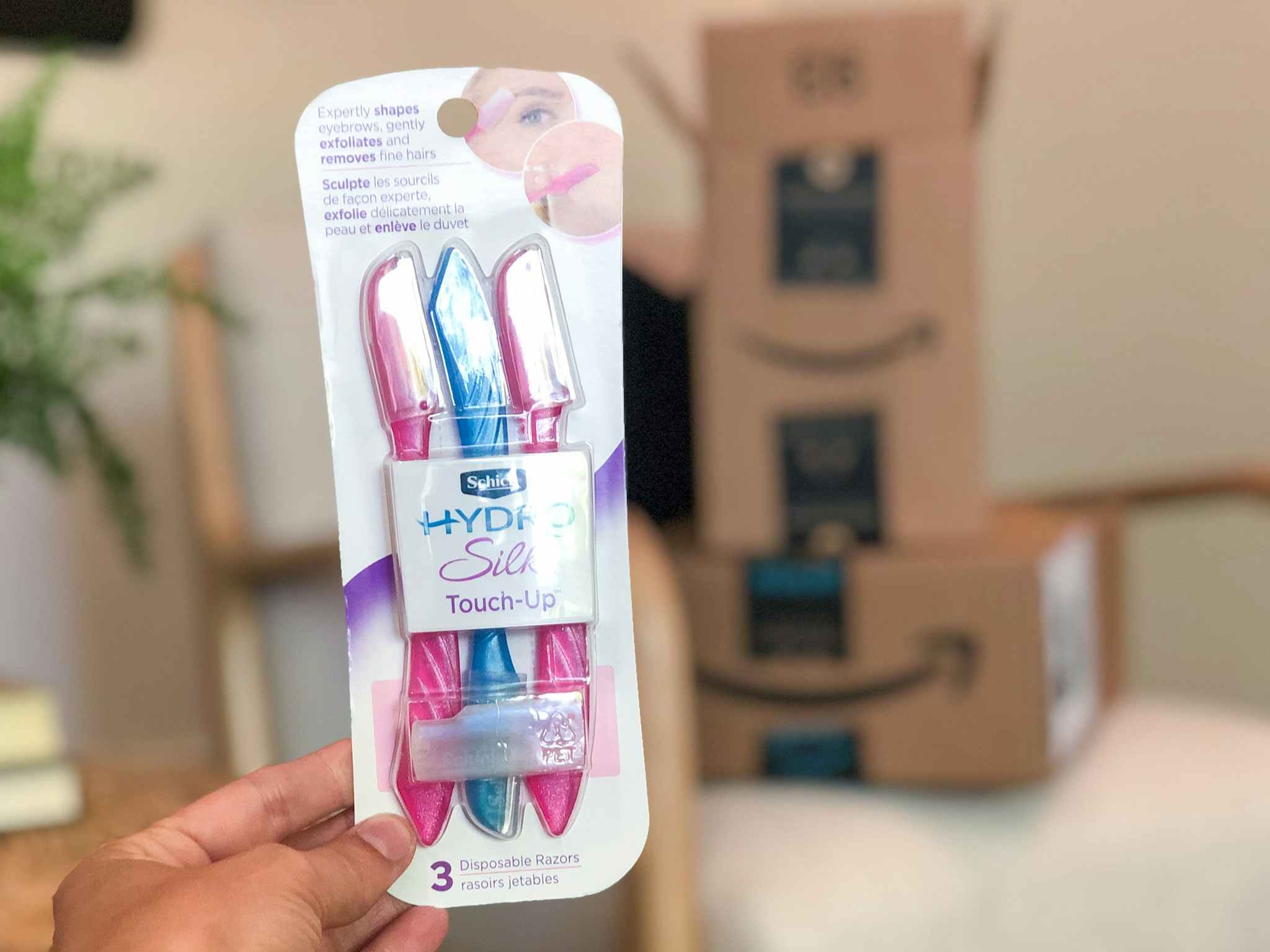 A hand holding Schick razors in front of Amazon boxes