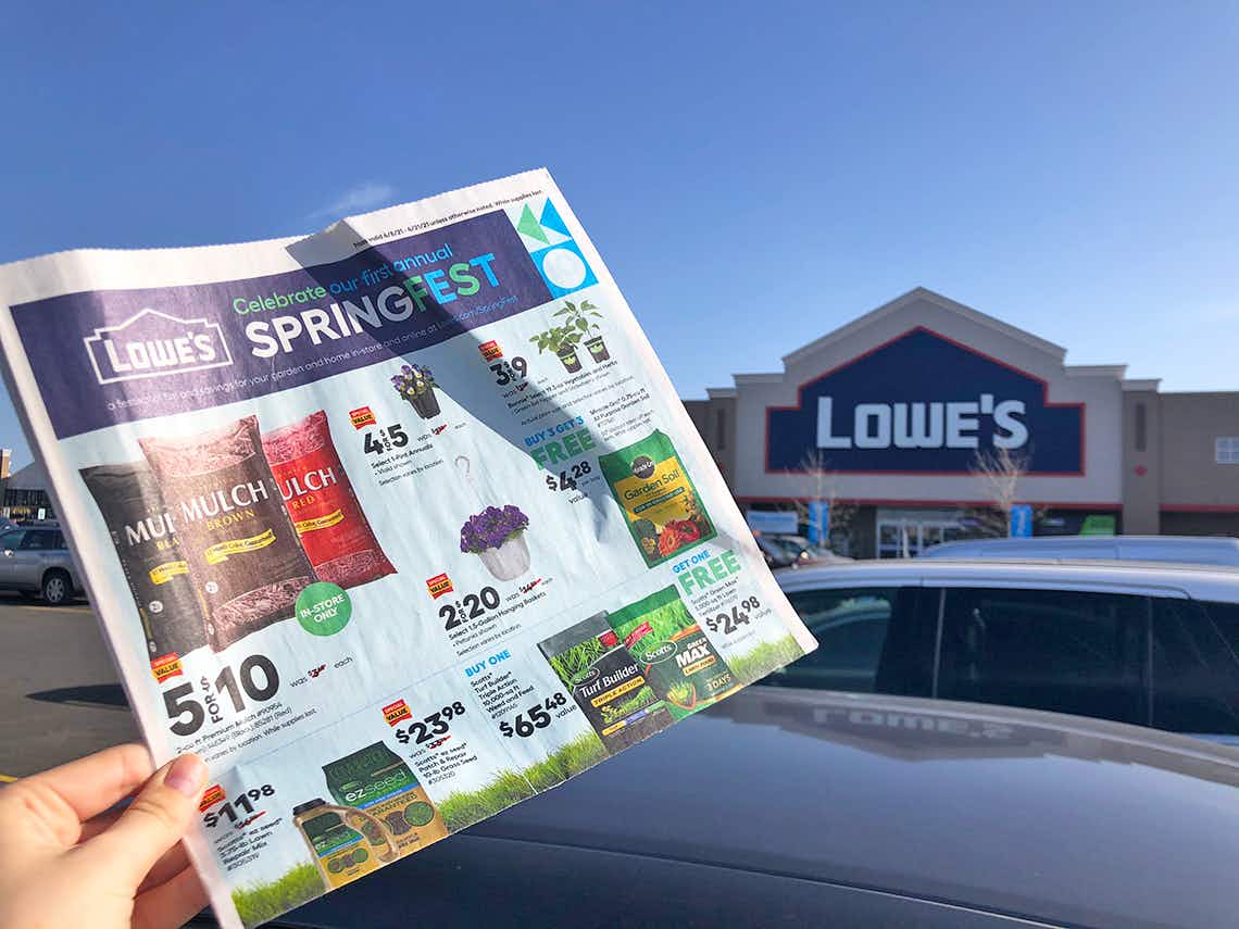 Someone holding up a Lowe's Springfest advertisement in front of a Lowe's