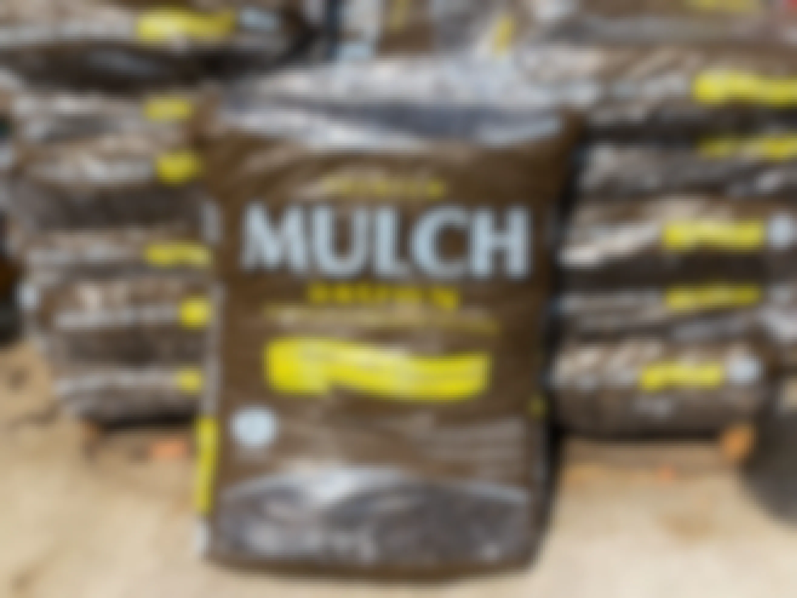 A bag of Premium brown mulch sitting on the ground in front of a pallet full of more bags of mulch in the Lowe's Garden Center