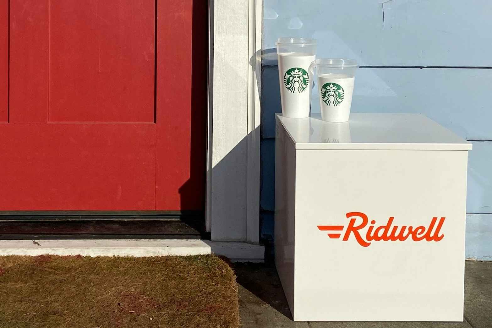 Two Starbucks cups on a box that said Ridwell next to a red front door.