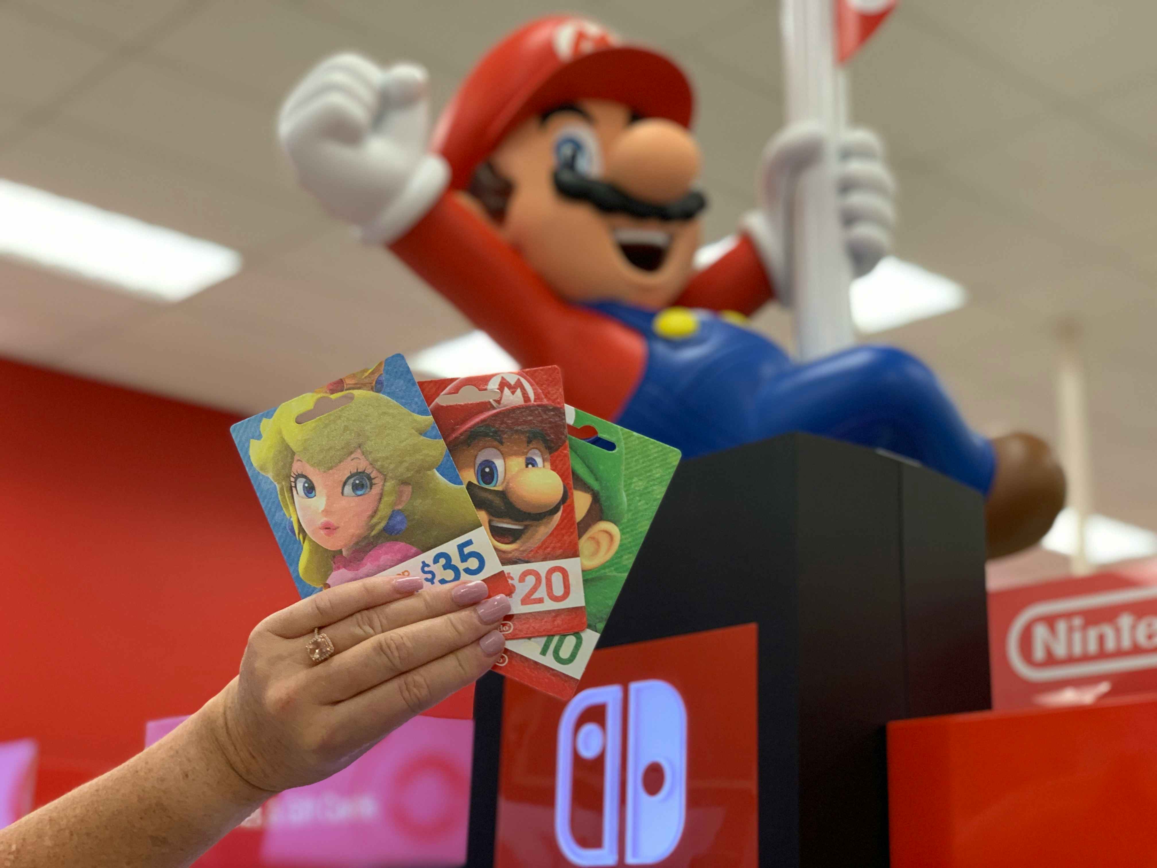 hand holding nintendo gift cards in front of Mario display