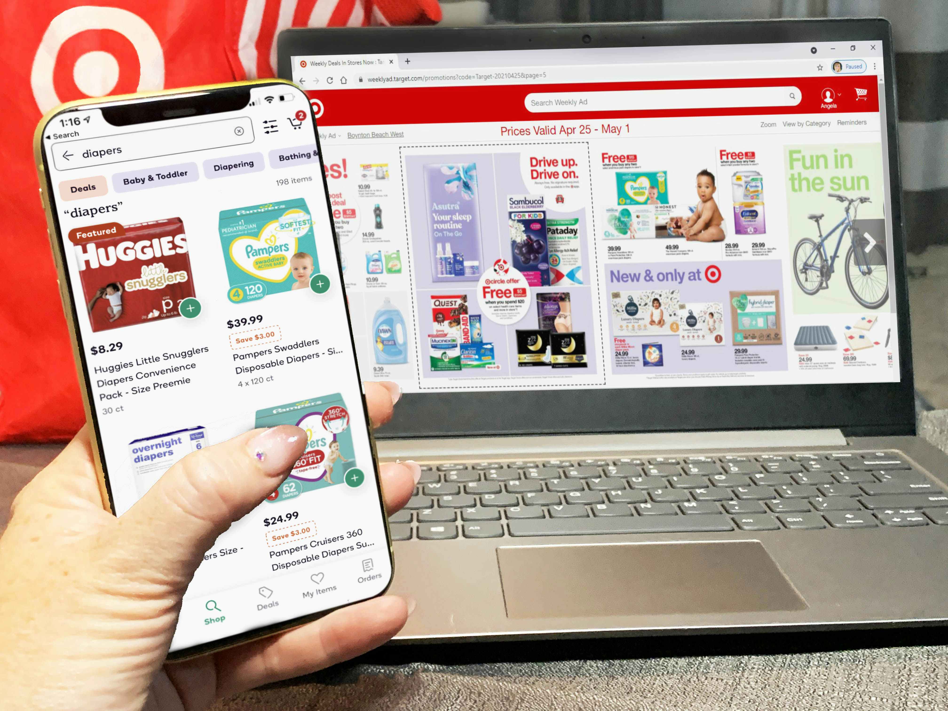 A person's hand holding their phone displaying the Shipt app's results for diapers at Target in front of a laptop displaying Target's weekly ad.
