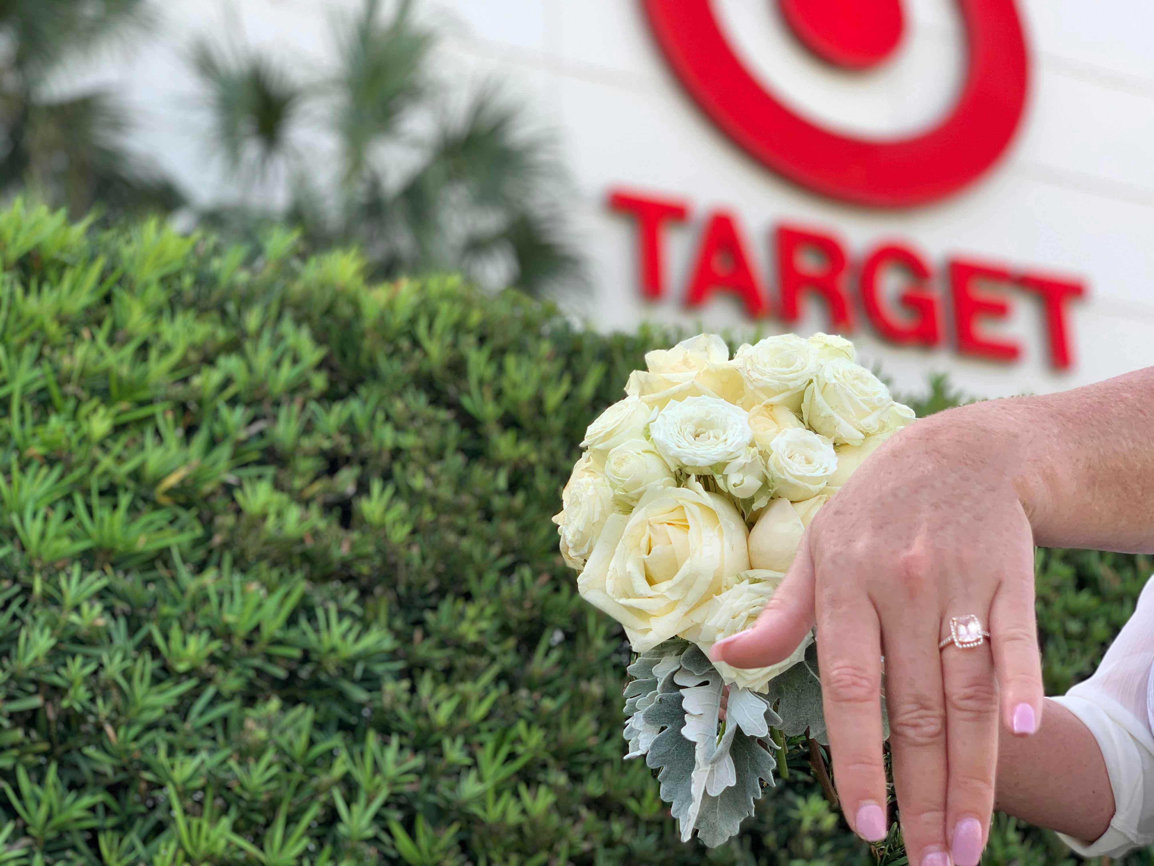 hand holding out wedding ring in front of white bridal bouquet in front of target store sign