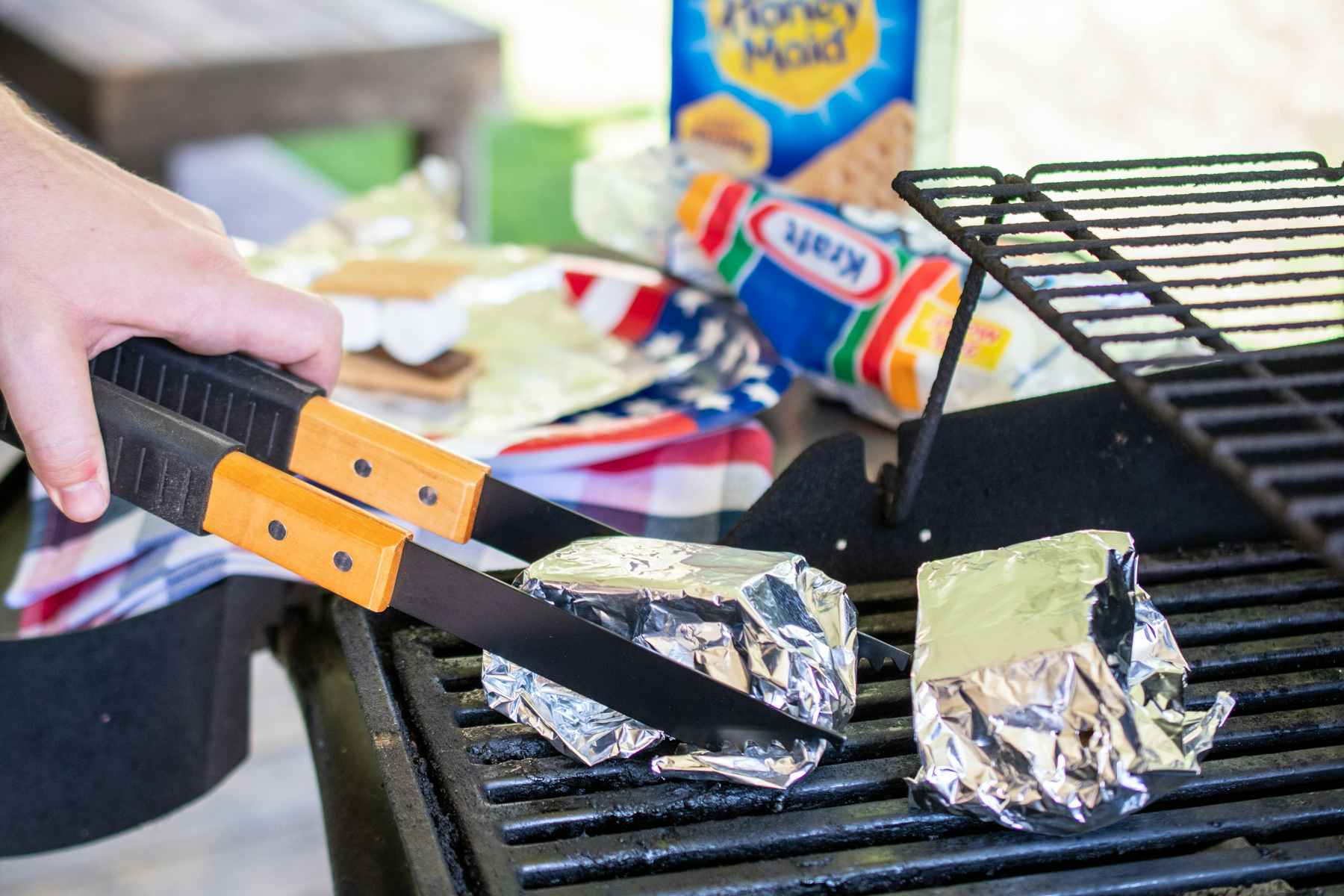 A person removing a tinfoil wrapped smore from a bbq