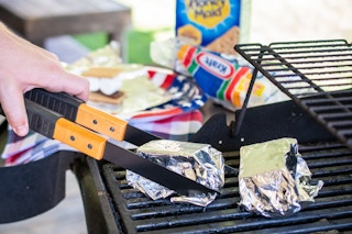 A person removing a tinfoil wrapped smore from a bbq