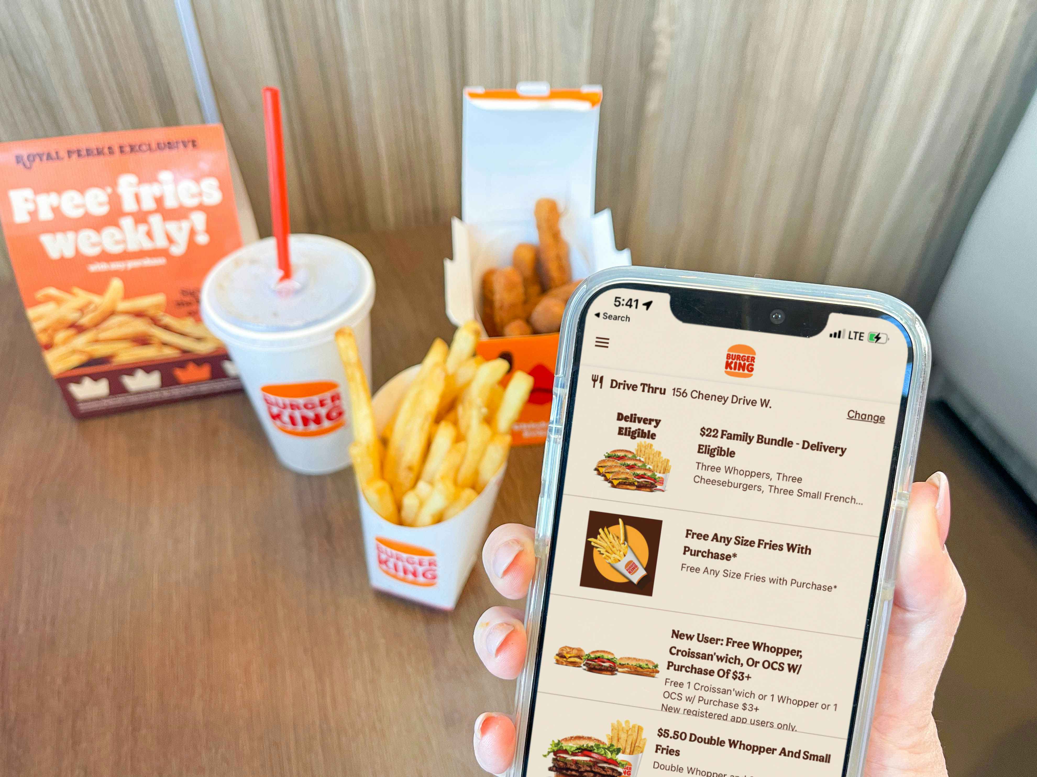 a hand holding cell phone with burger king app being held in front of fast food sitting on the table