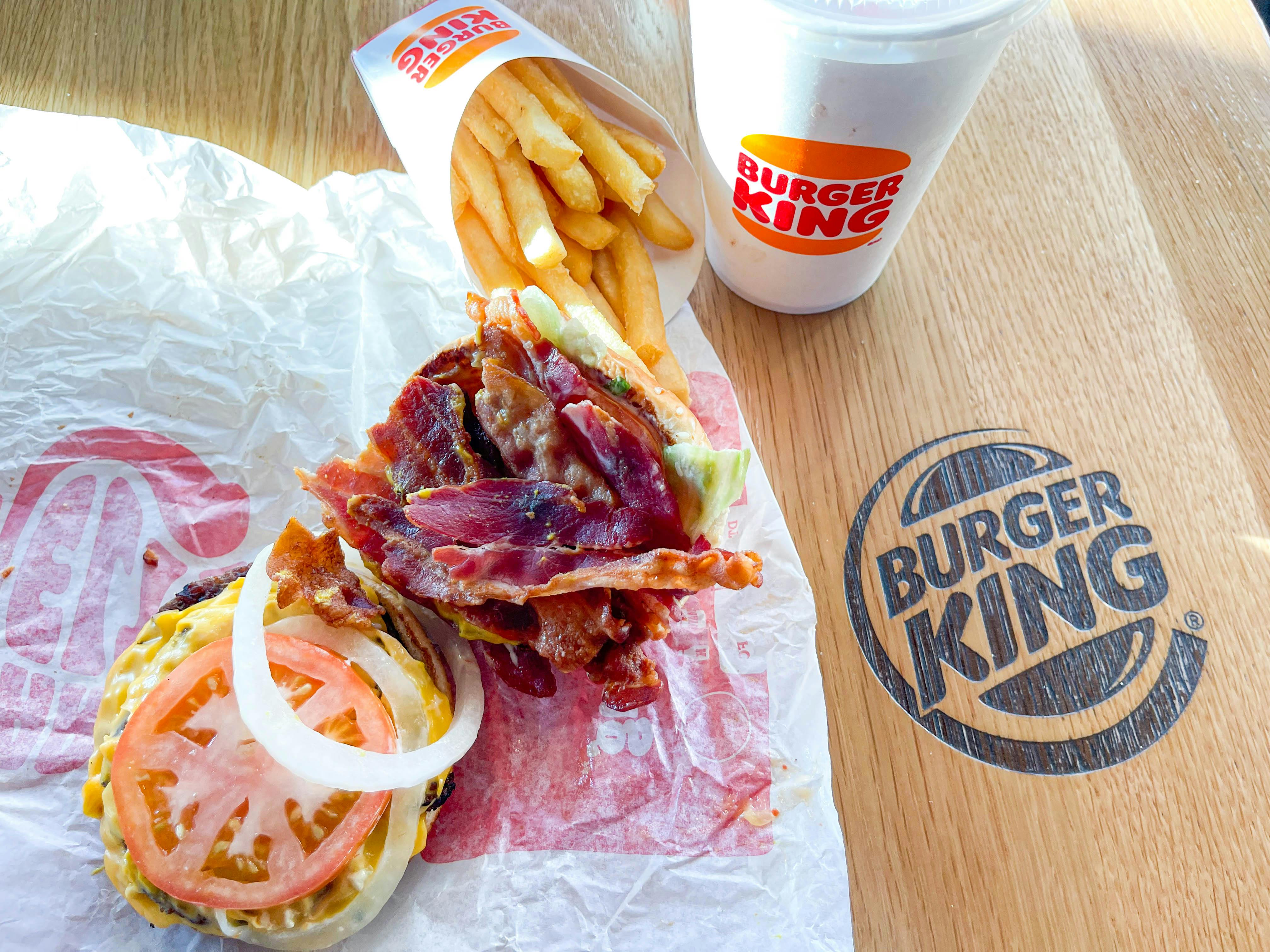 burger king burger on table with extra bacon near fries and drink