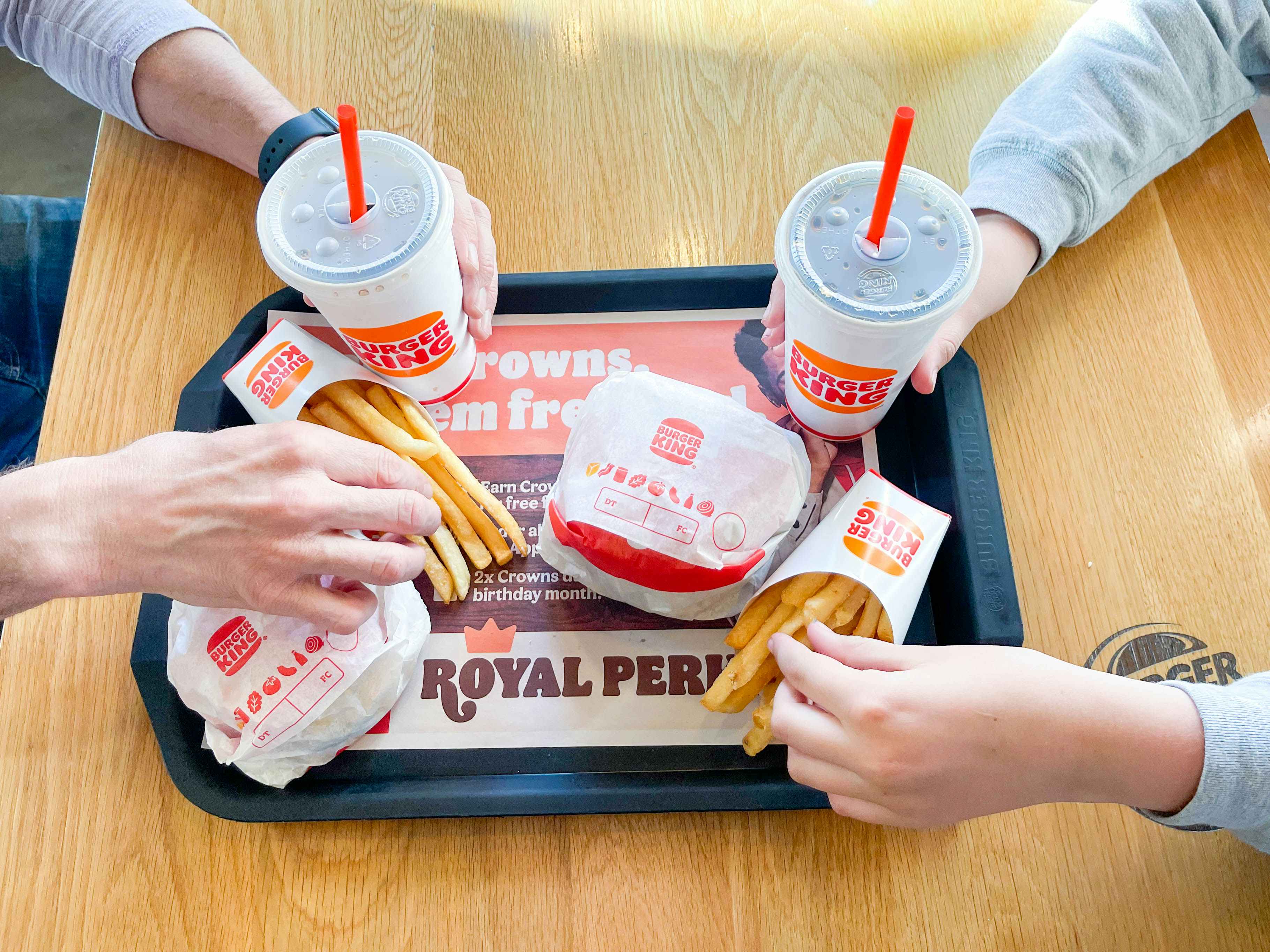 a tray with 2 burgers, 2 fries, and 2 drinks being grabbed by two people