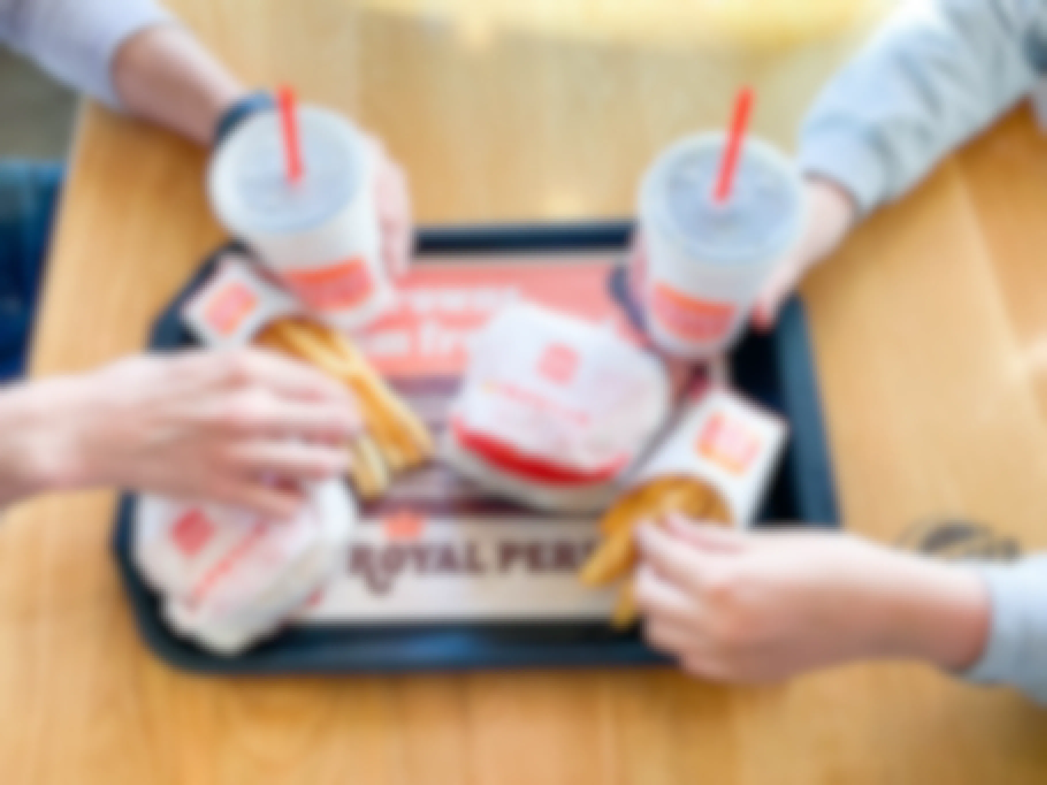 a tray with 2 burgers, 2 fries, and 2 drinks being grabbed by two people