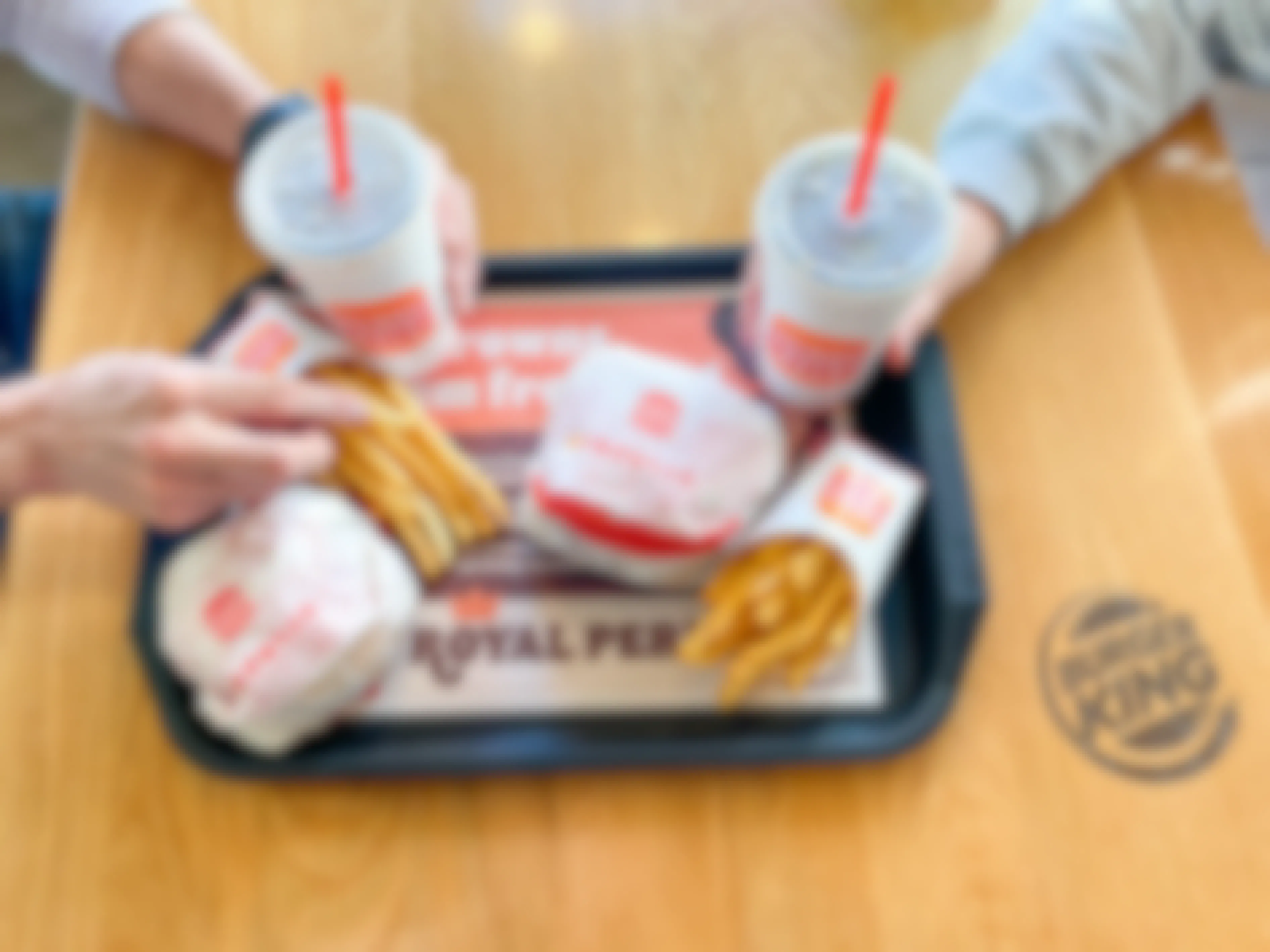a tray with 2 burgers, 2 fries, and 2 drinks being grabbed by two people