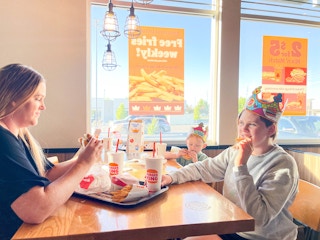 a woman and two kids eating at a table inside burger king