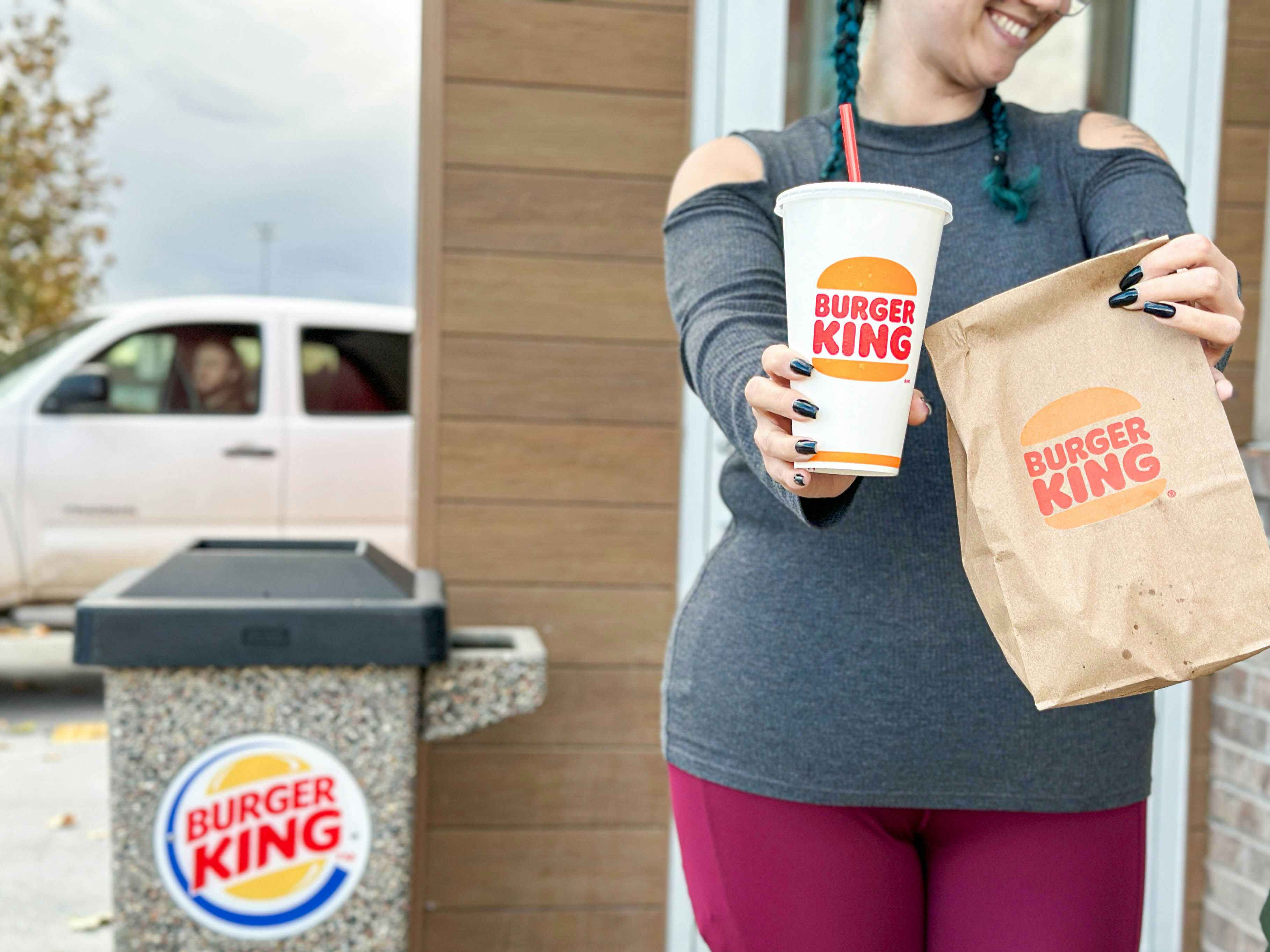 a woman holding out a burger king drink 