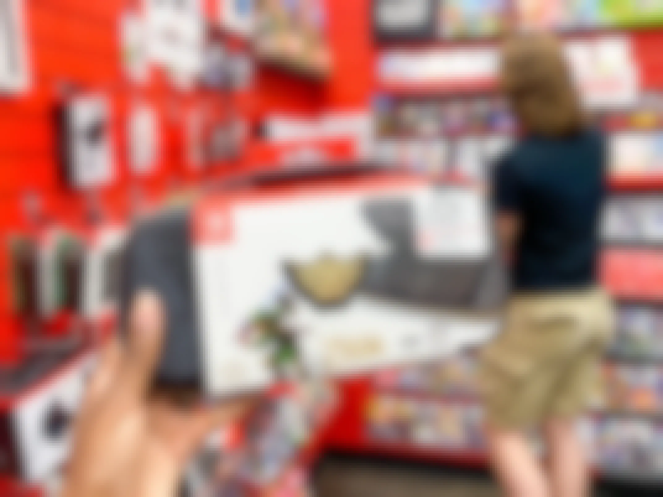 A person's hand holding up a Nintendo Switch Legend of Zelda carrying case inside a GameStop store with someone looking at games in the background.