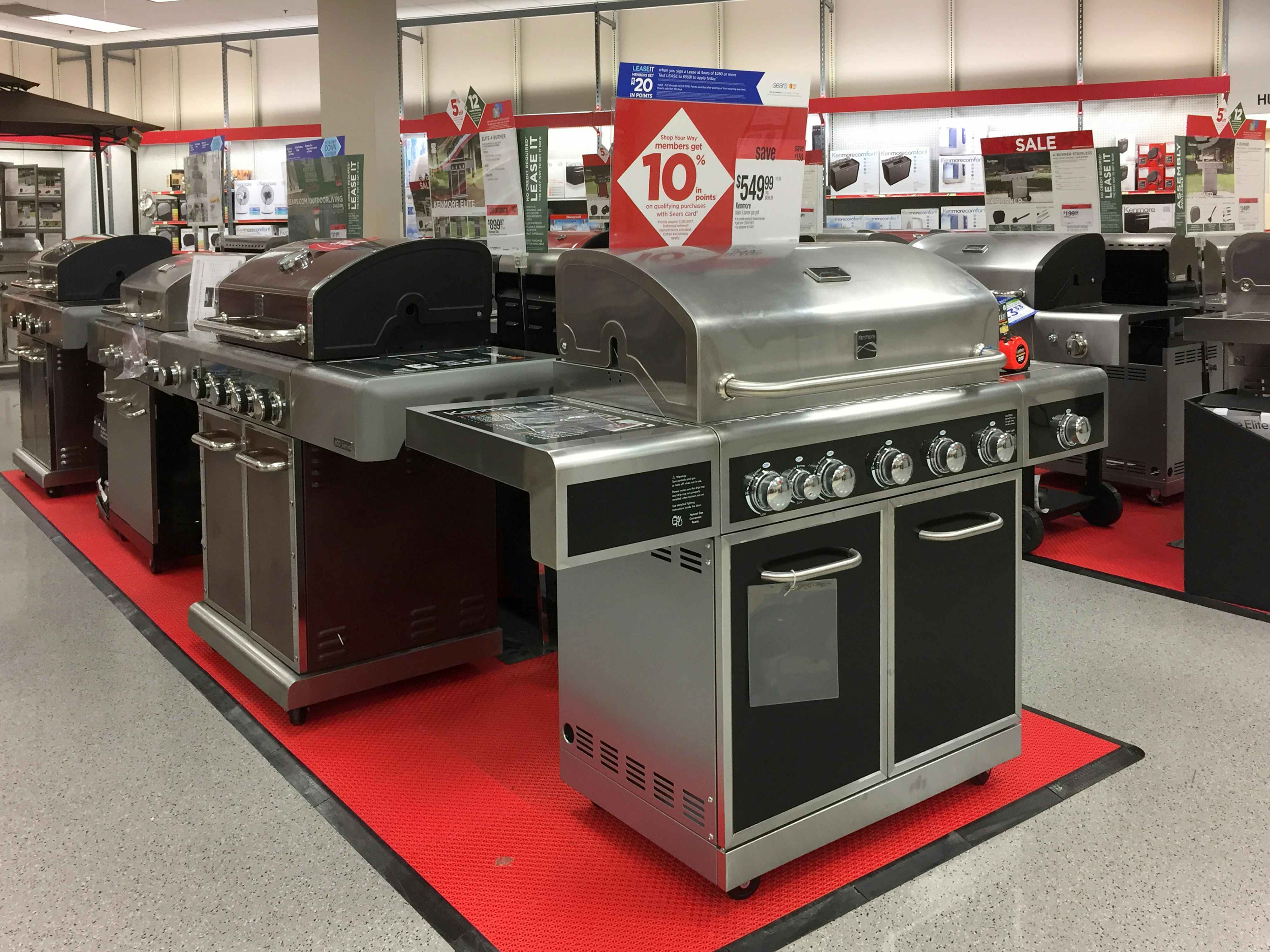 Row of grills. The first one is facing the camera and the rest are to the side. There is a sign above the first grill that has 10% written on it and a price tag that says $549.99
