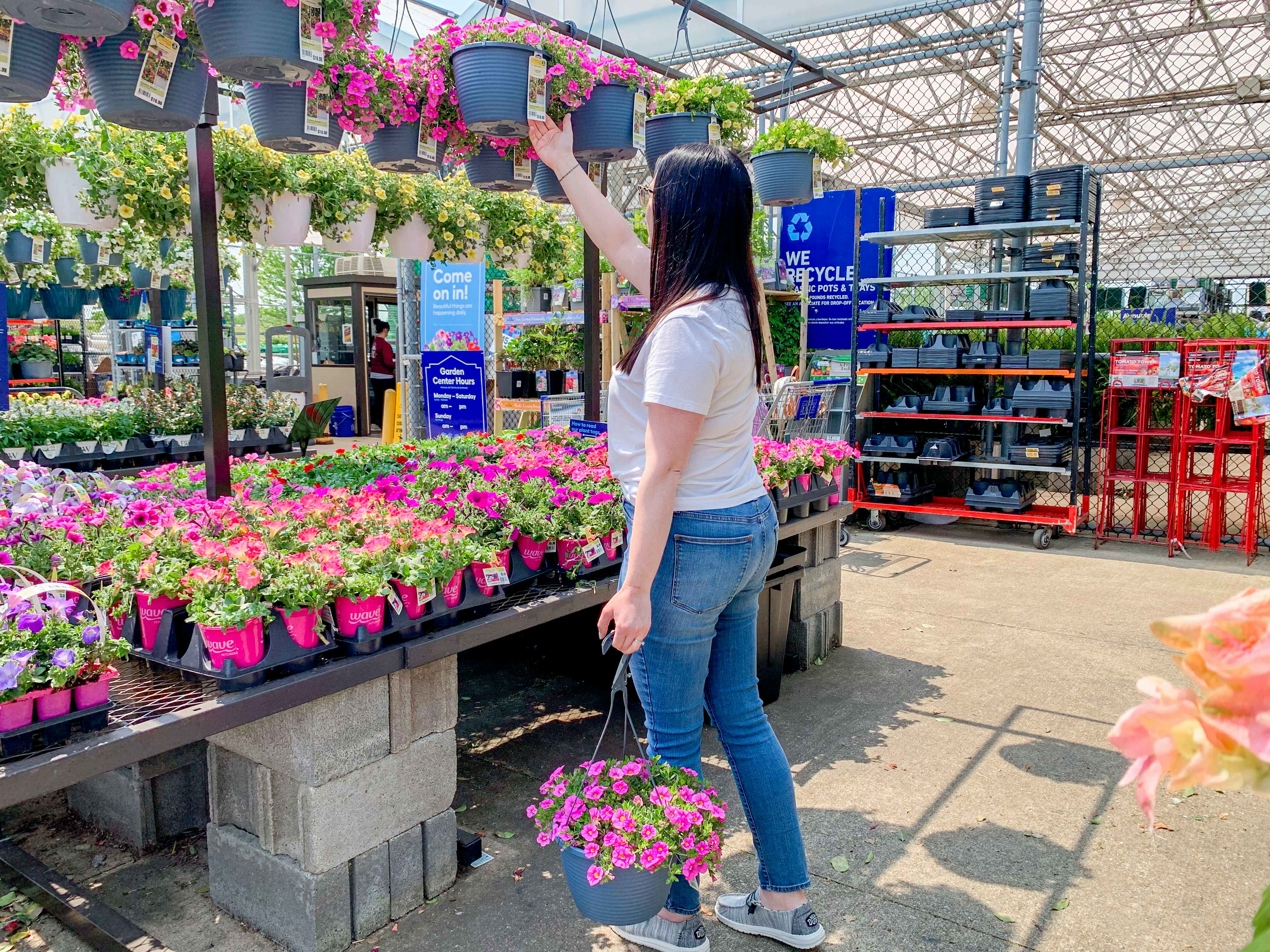 a person holding a hanging basket while reaching for another hanging basket at lowe's