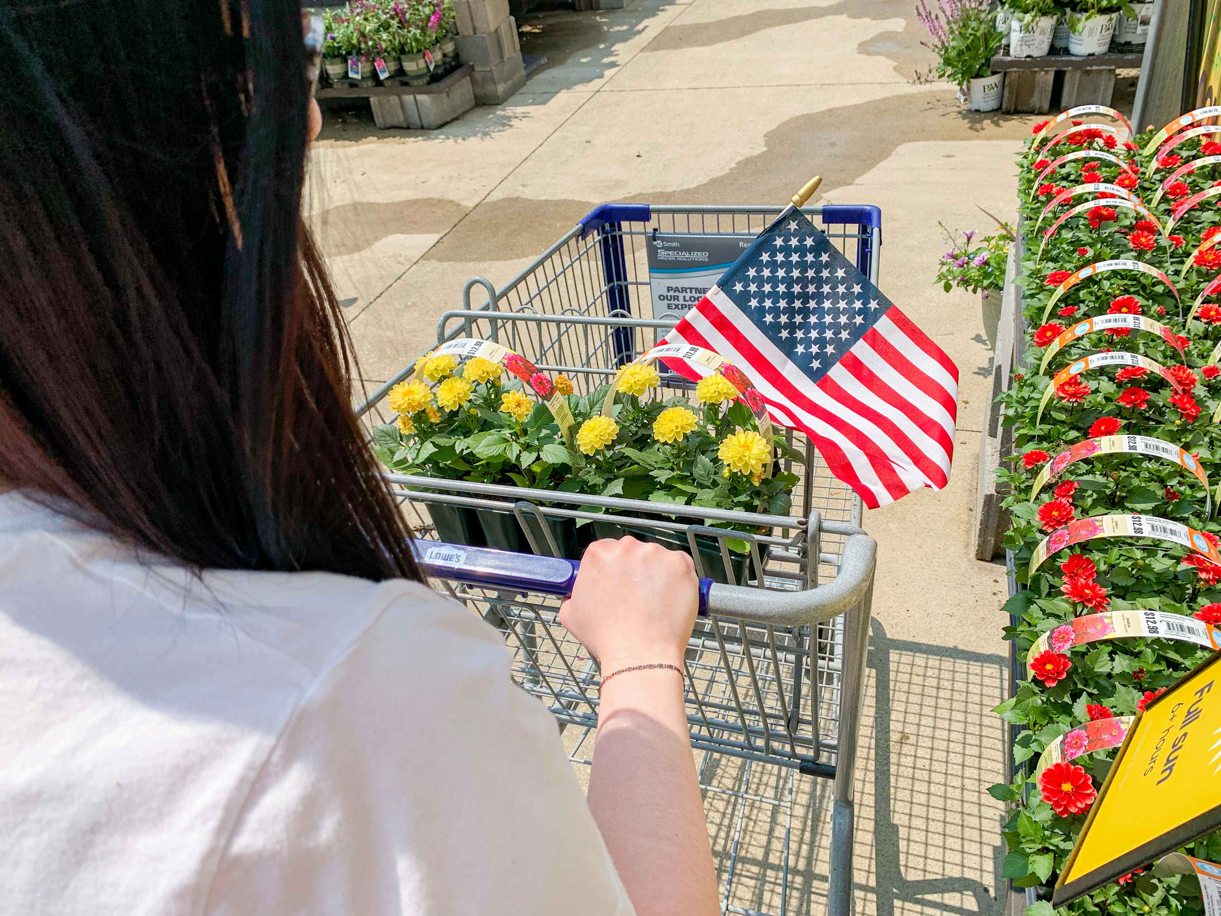 a person pushing a cart full of flowers and an american flag at lowe's