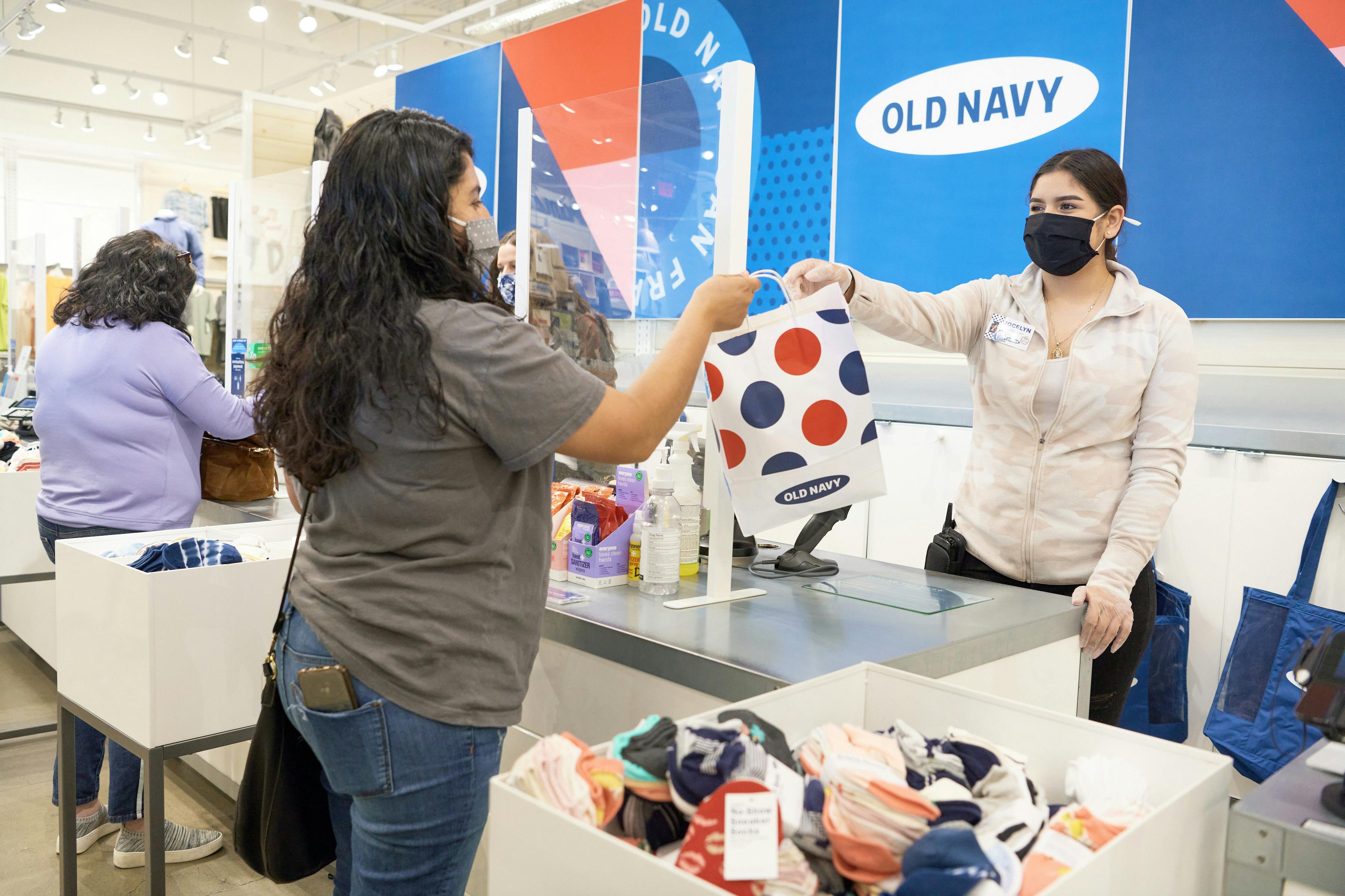 An Old Navy employee handing a customer her bag over the checkout counter at Old Navy.
