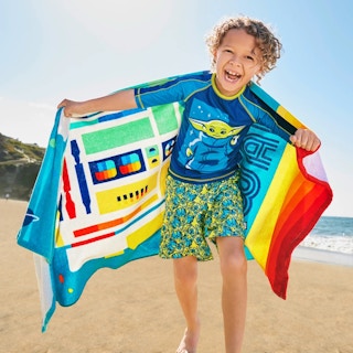 Little boy in Star Wars swim outfit running on beach and laughing.