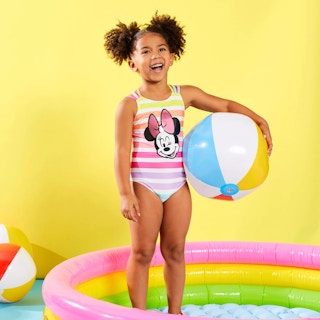 Little girl in swimsuit standing in kiddie pool holding a beach ball.