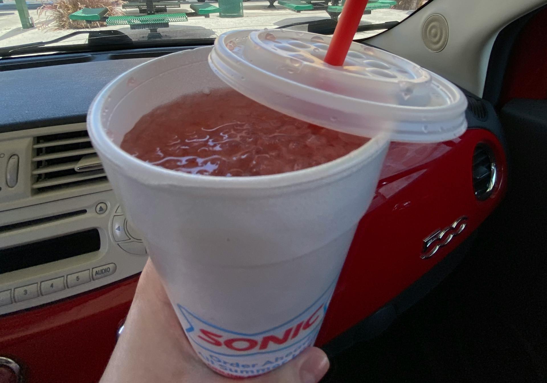 A person's hand holding a Sonic drink cup with the lid removed to show the drink.