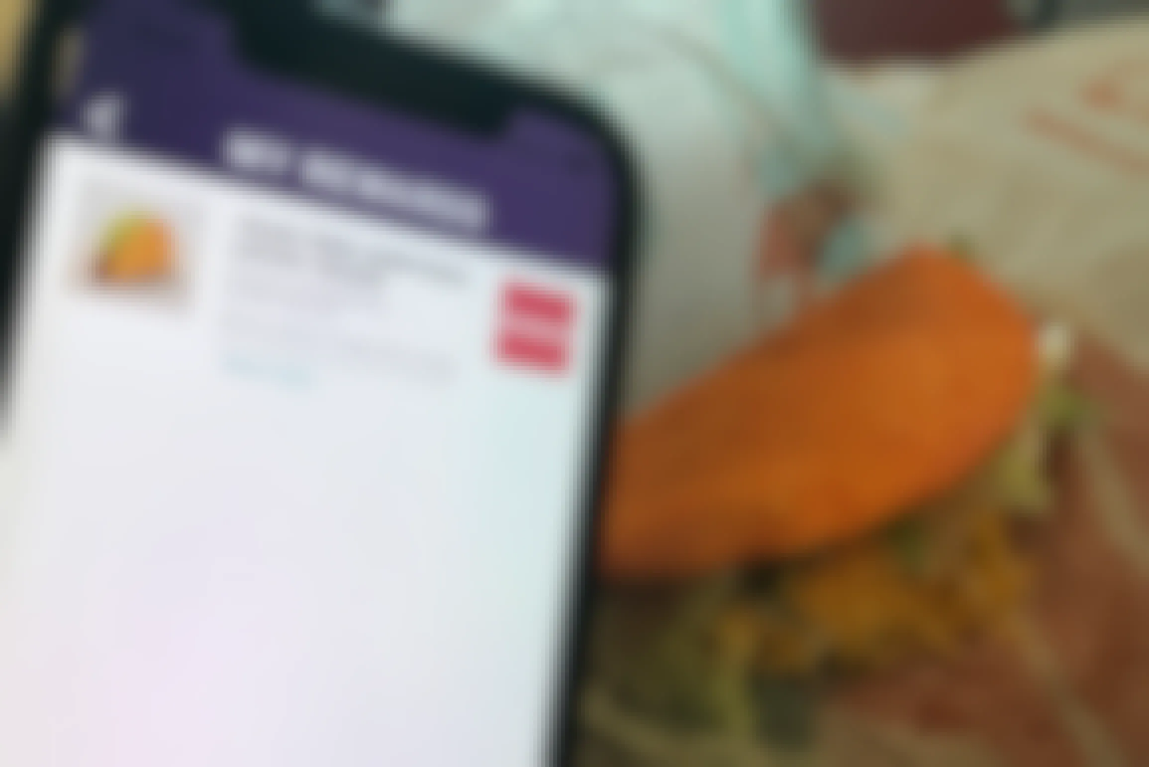 A cell phone displaying the Taco Bell app's My Rewards page, with a reward for a free Doritos Locos Tacos, being held in front of a Doritos Locos Tacos sitting on its paper wrapper.