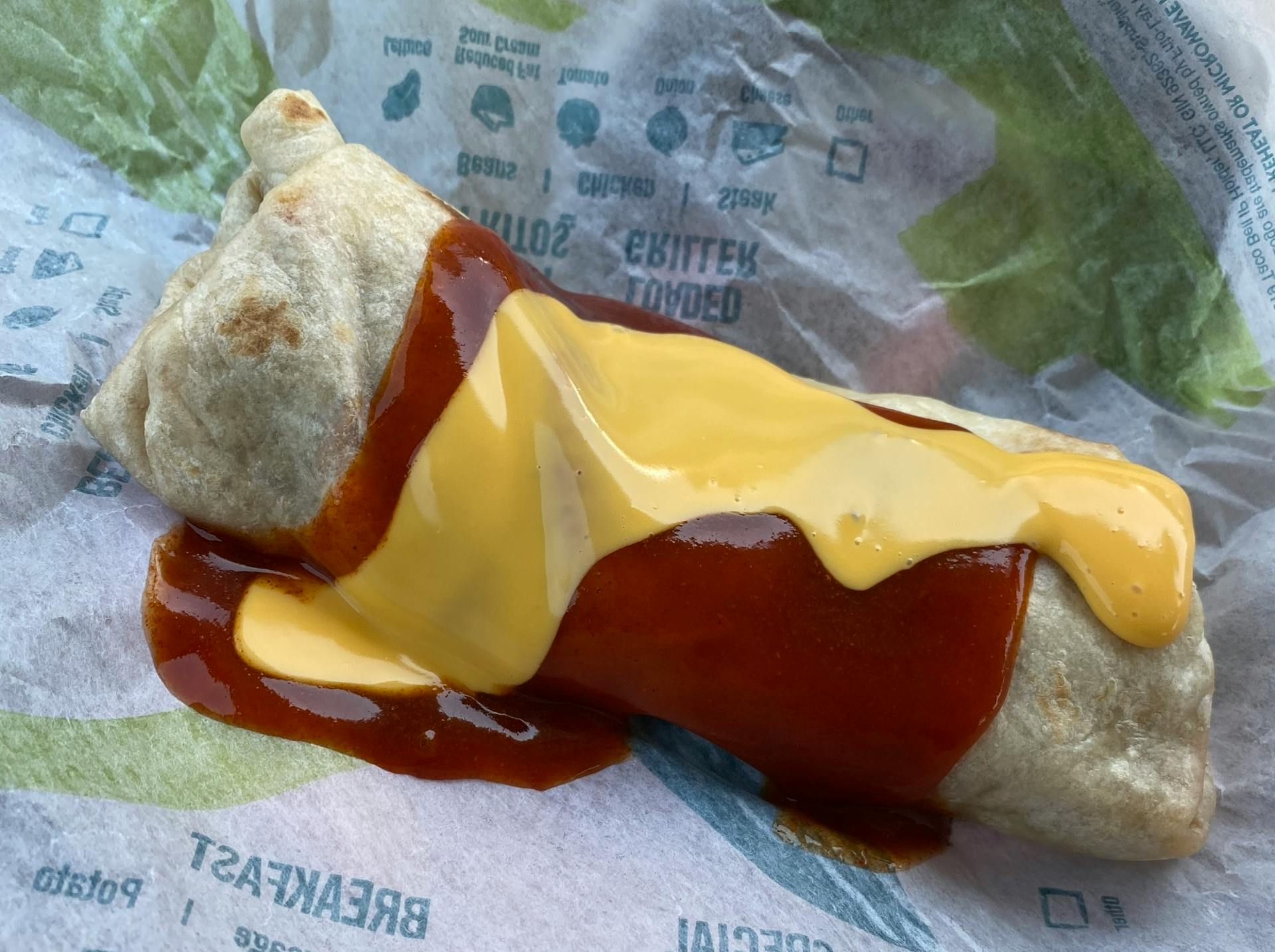 A close-up of a Taco Bell Enchirito sitting on its paper wrapper.