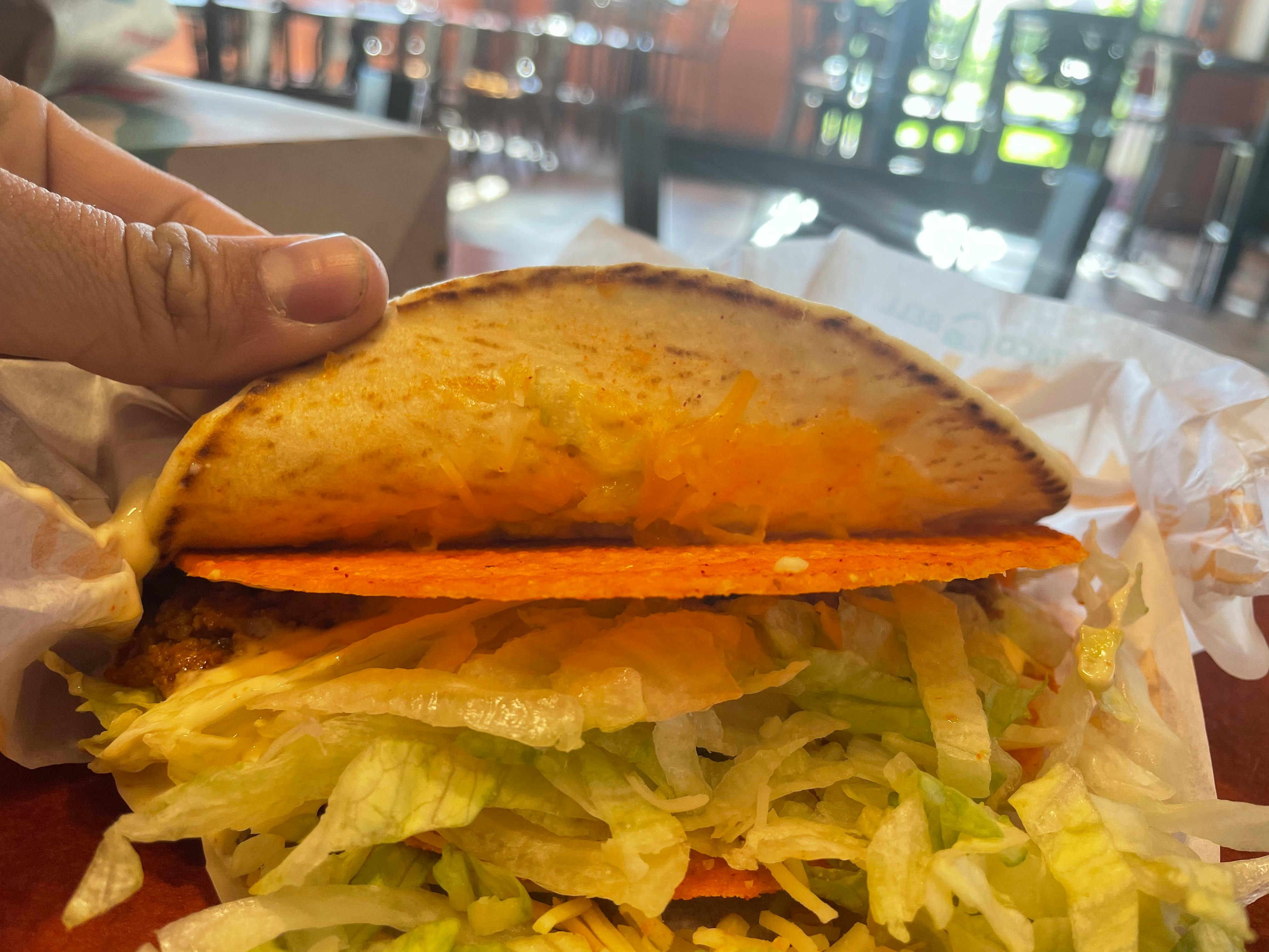 A person's hand lifting a tortilla of a Taco Bell taco to reveal a Dorito shell inside.