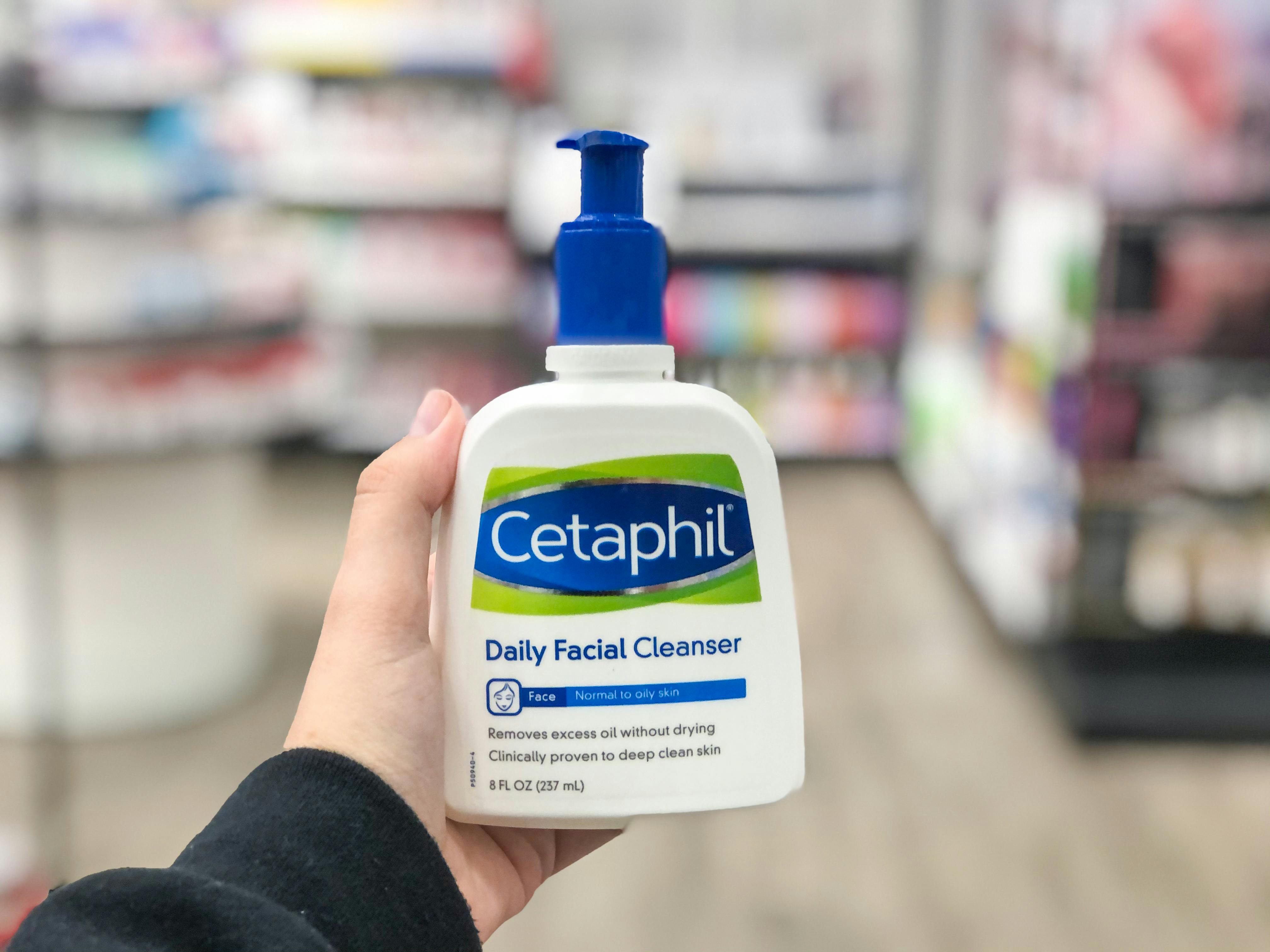 A person's hand holding a pump bottle of Cetaphil Daily Facial Cleanser in an aisle at Target..