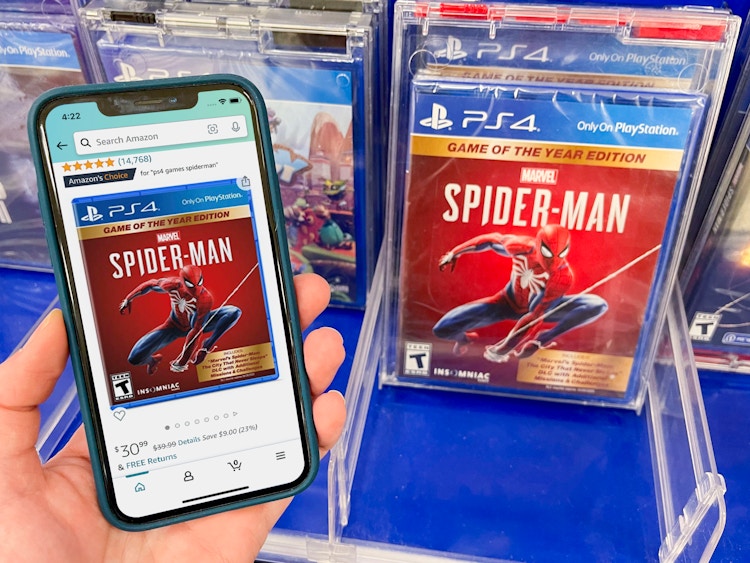 A Sony Spiderman game on a shelf at Target. A cell phone displaying the price on the game from Amazon held next to it.