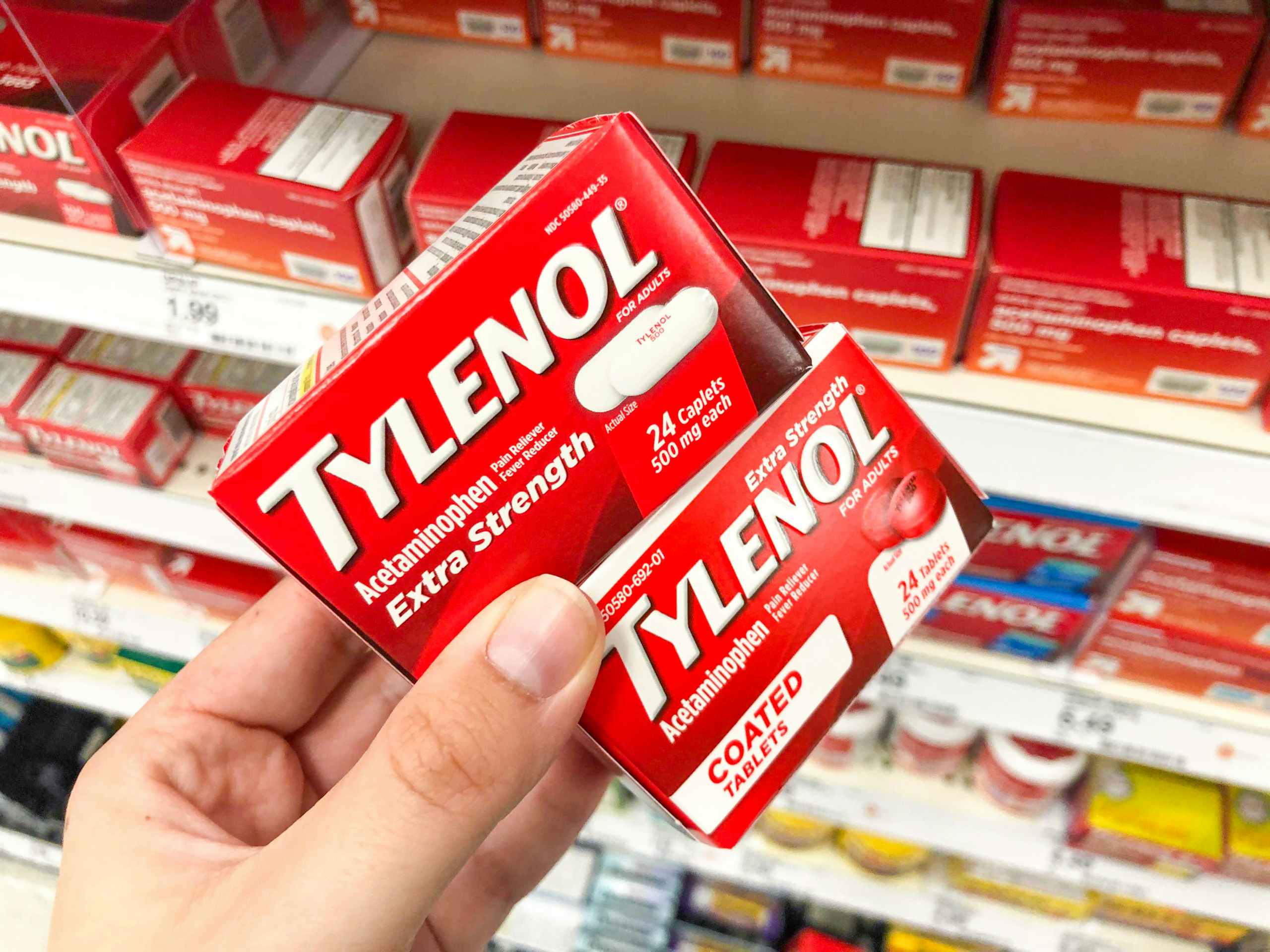 hand holding two tylenol boxes in front of shelf