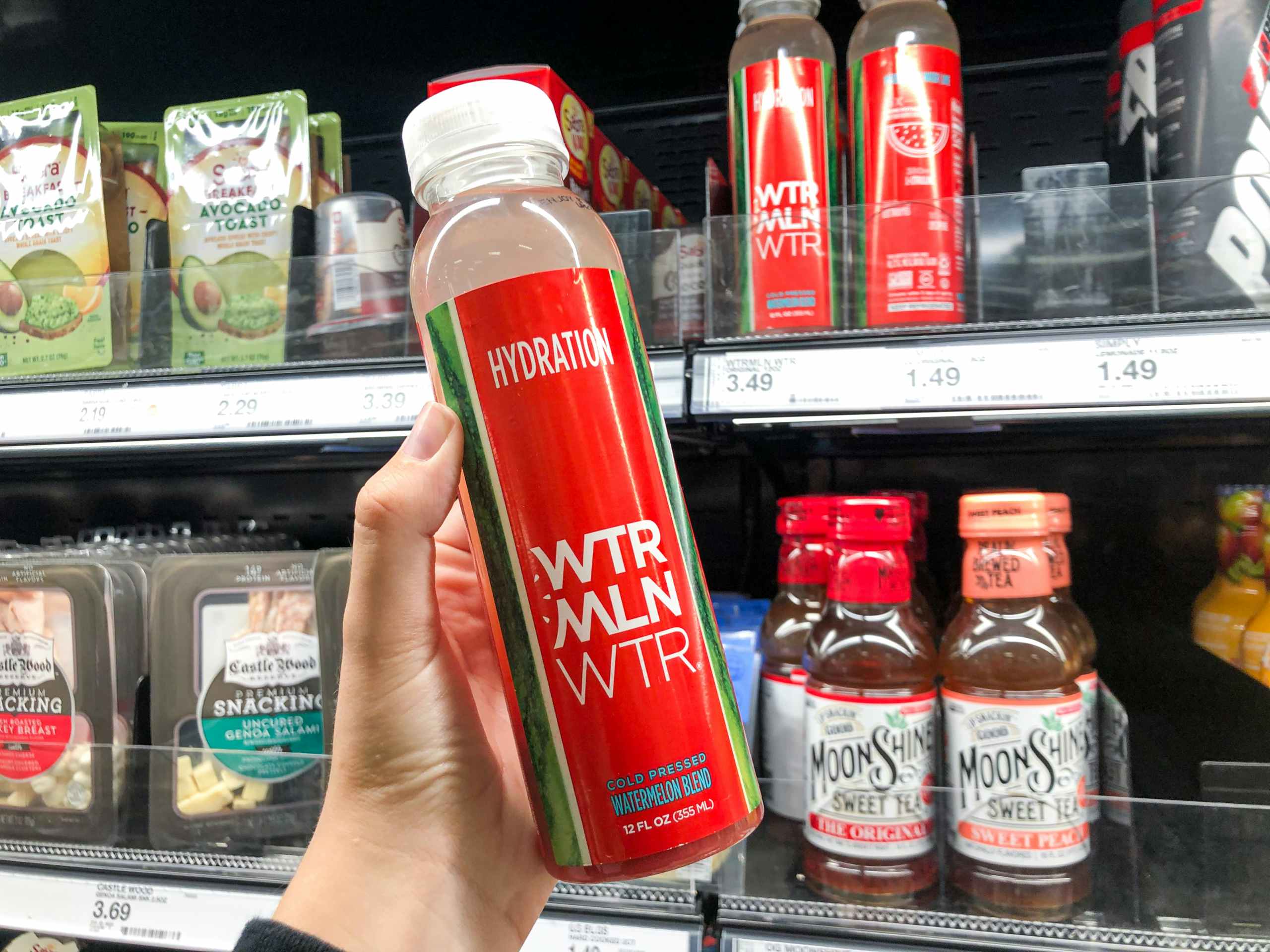 hand holding bottle of water melon water in front of store cooler