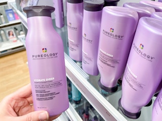 Woman holding bottle of Pureology shampoo.