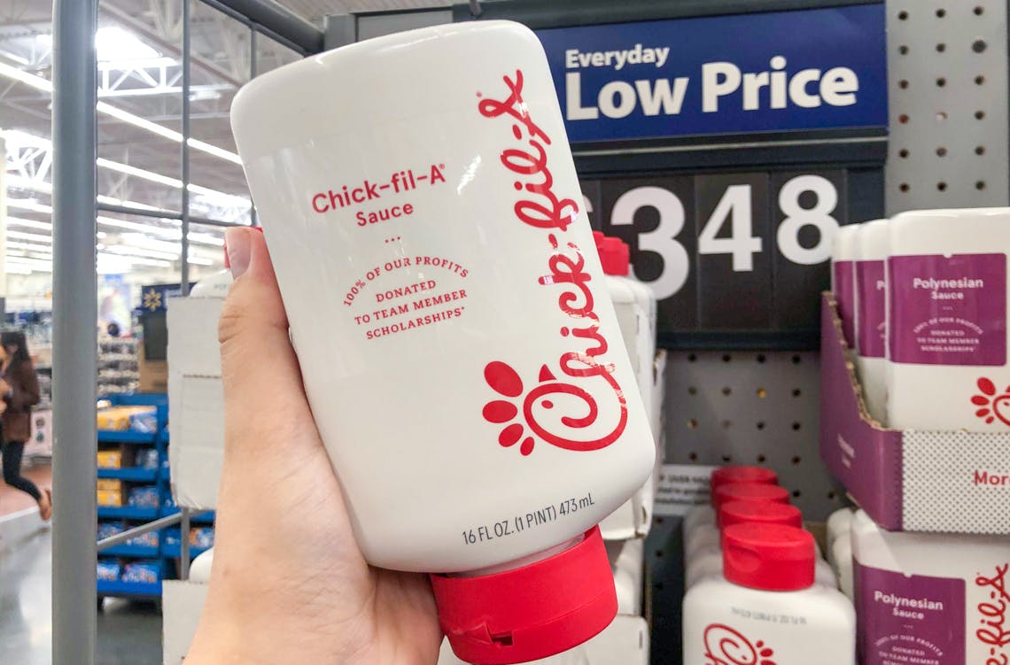 A person's hand holding a bottle of Chick-fil-A sauce in front of a shelf with more of the same product at Walmart.